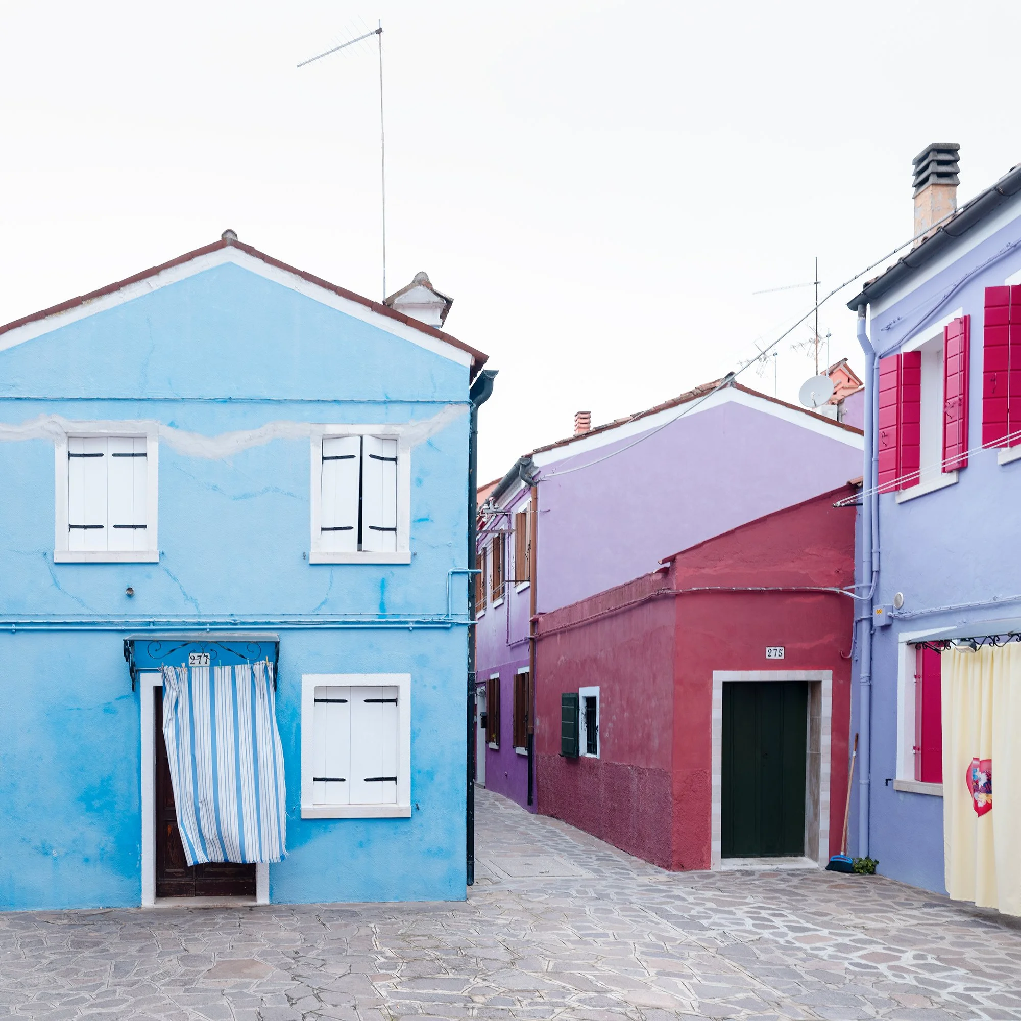 © 2025 Gerald Berghammer photo - Colorful houses in pastel shades on a cobblestone street, with colorful windows and a striped curtain hanging in front of one house. Print detail 2