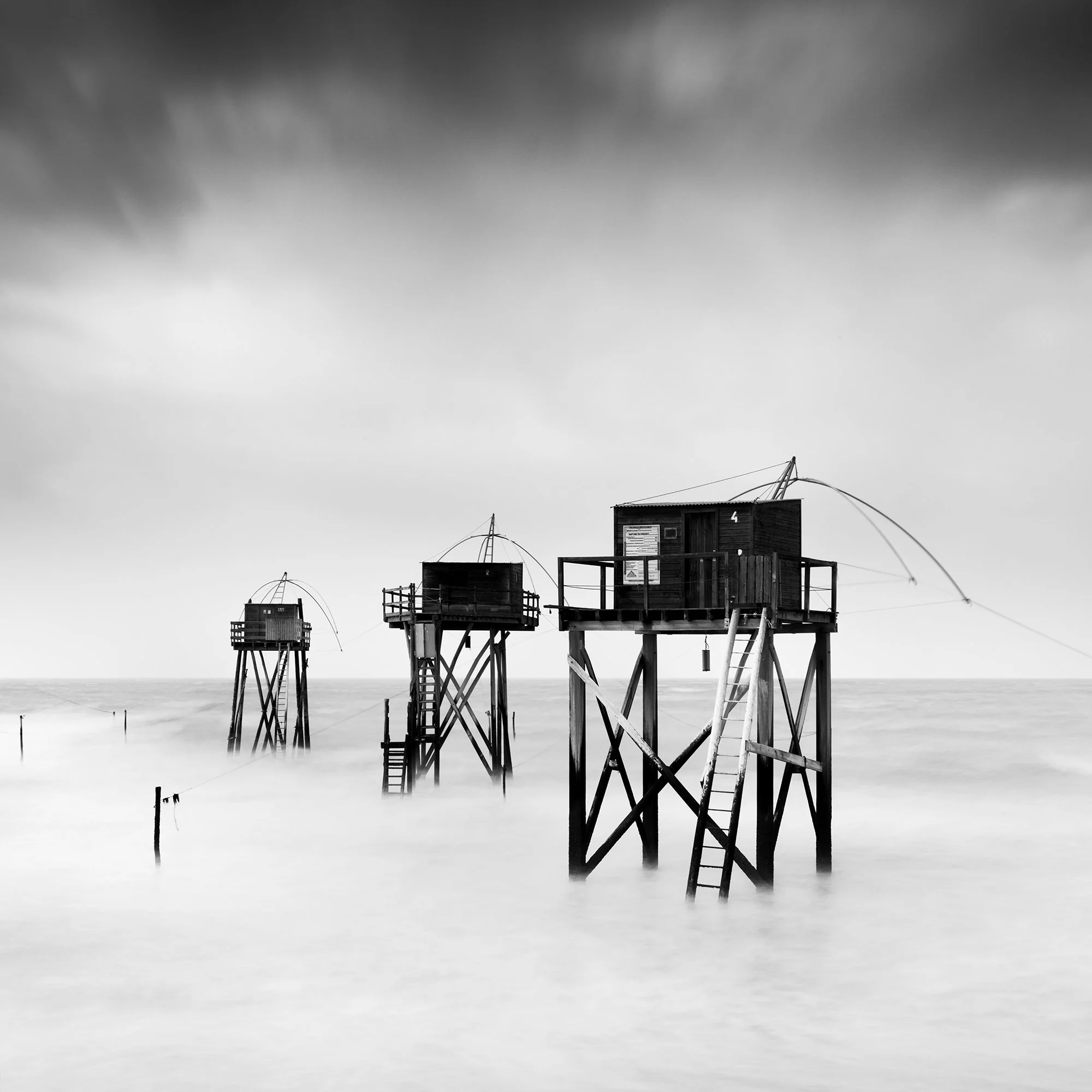 Monochrome long-exposure seascape with wooden fishing huts on stilts and misty water, Detail 1