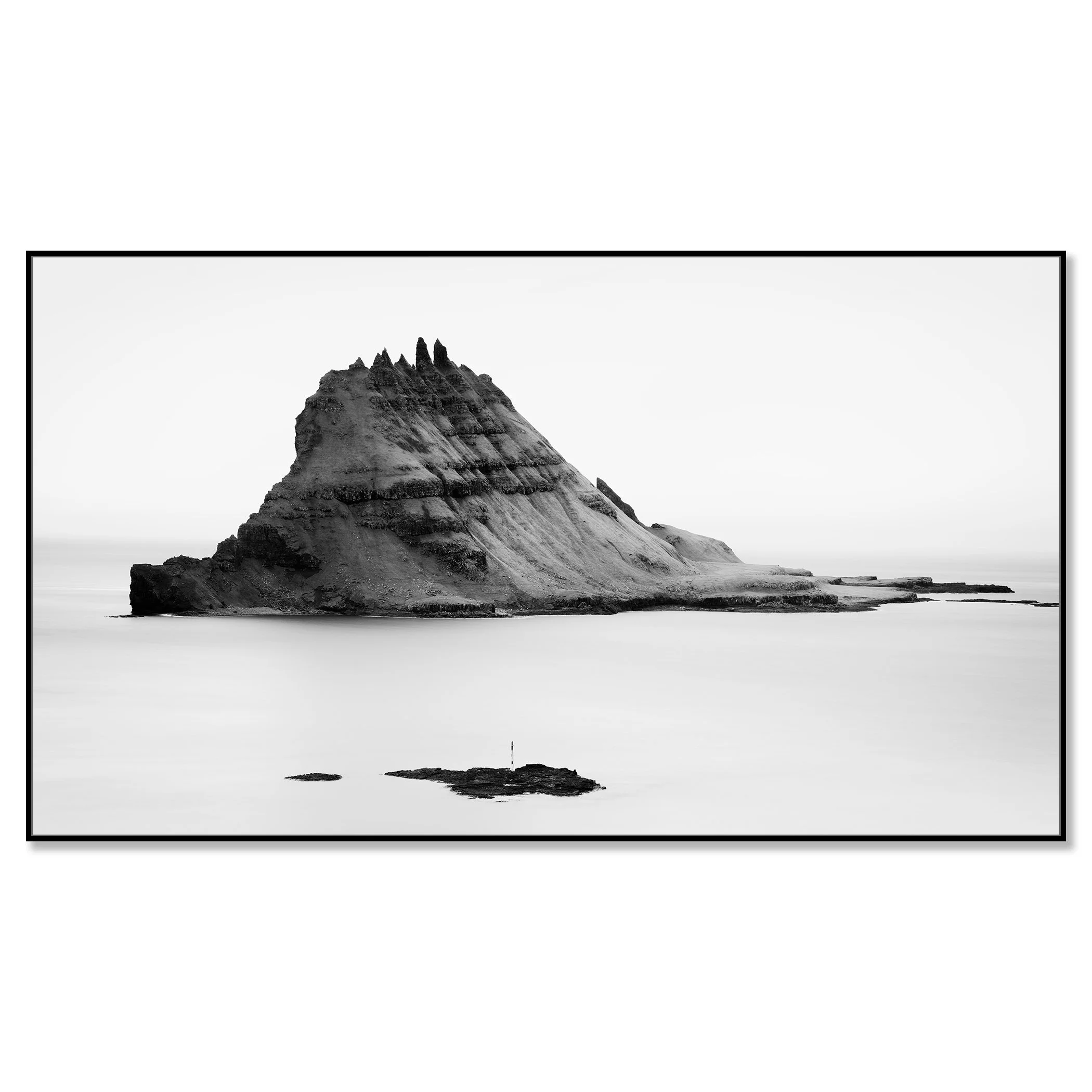 Black-and-white panoramic photo of a layered sea stack in the ocean, with smaller rocks in the foreground and waves – framed ArtBox black