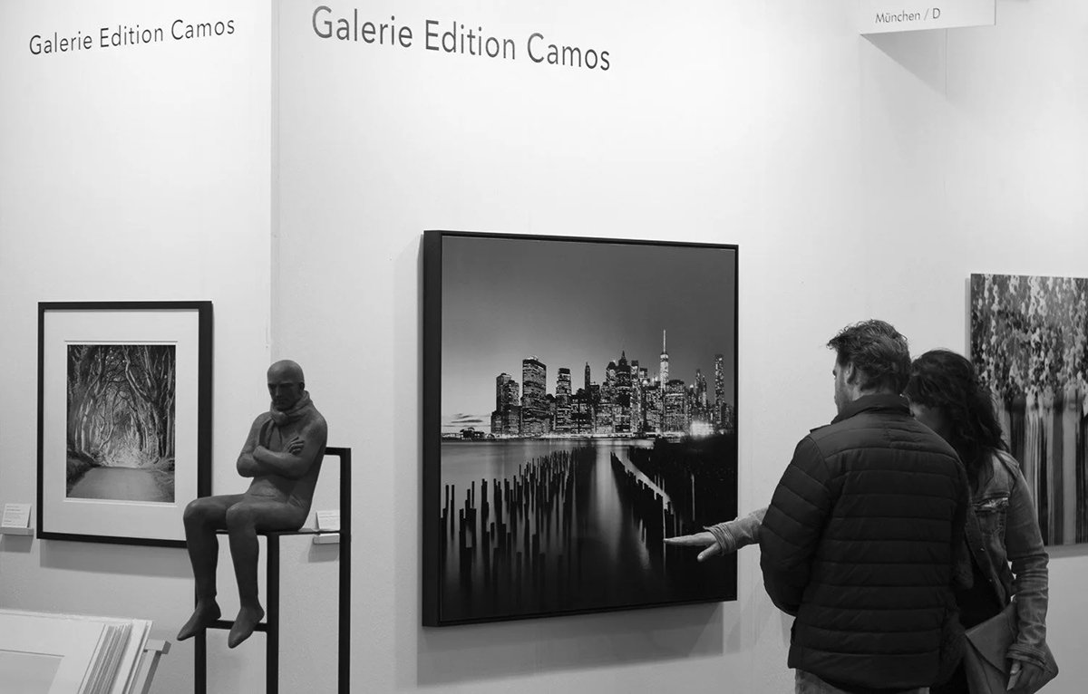 Galerie Edition Camos stand at art KARLSRUHE 2018 with a Manhattan skyline photograph by Gerald Berghammer, a sculpture and visitors.