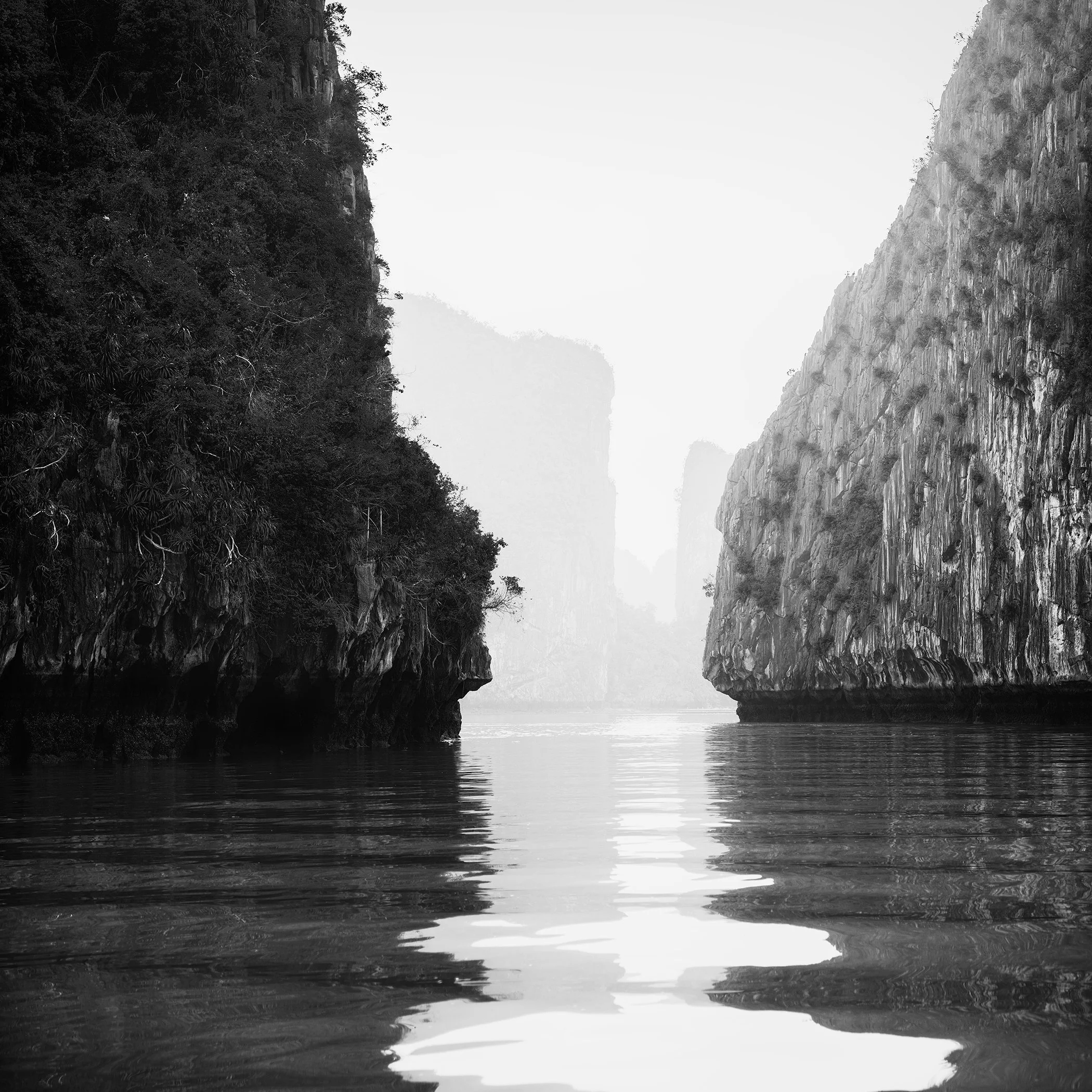Tranquil black-and-white fine art photograph of karst limestone cliffs reflected in calm water, Vietnam.