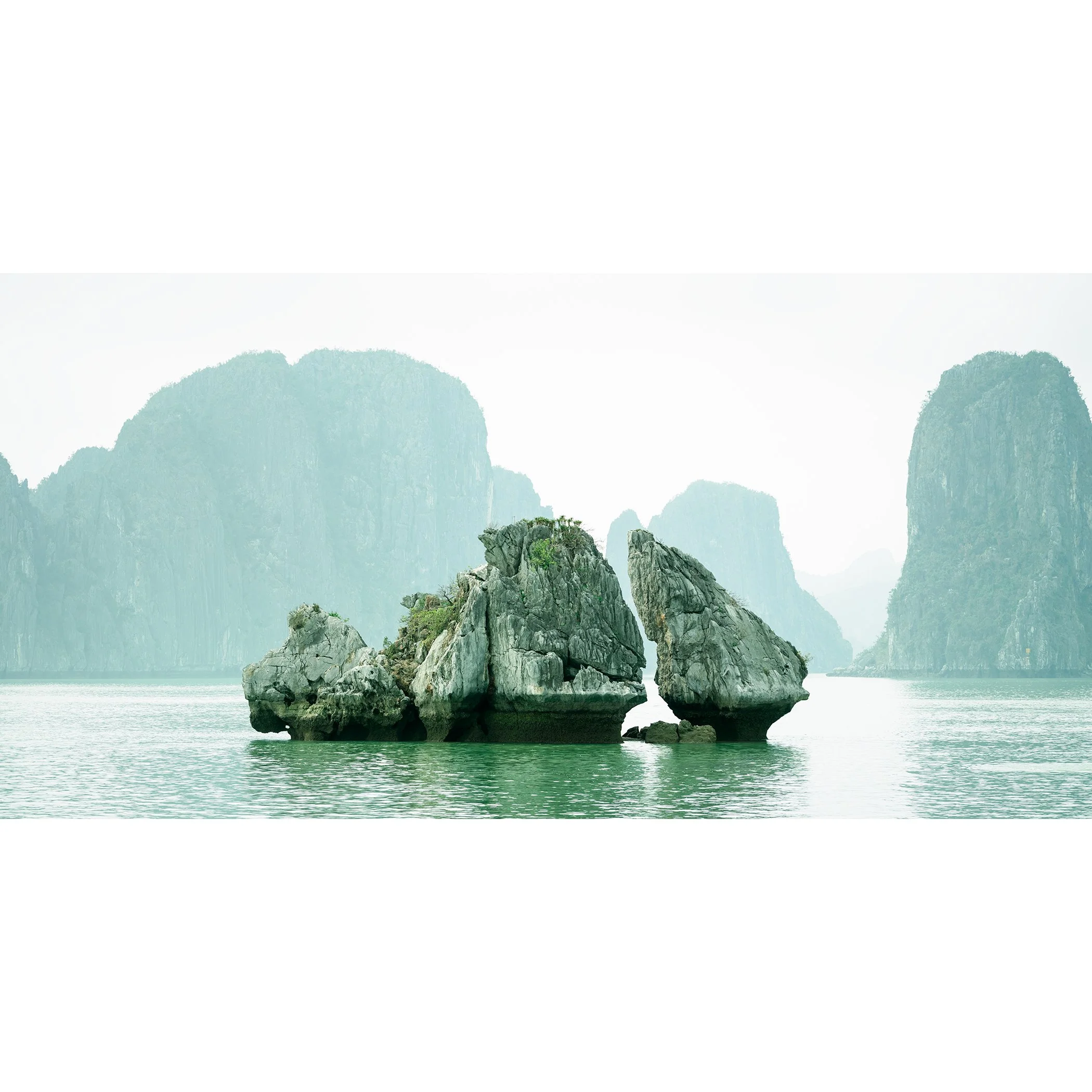 Gerald Berghammer - Color seascape photography. Large rocks rising from the water with, surrounded by calm water and distant limestone cliffs and islands.