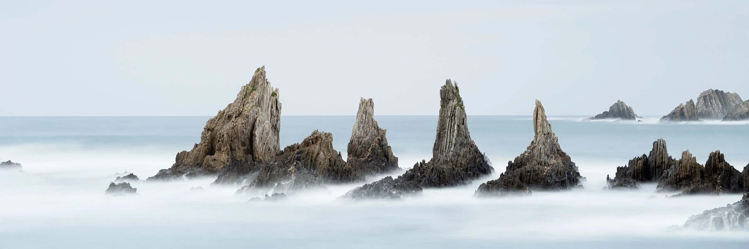 Panoramic long-exposure colour seascape of jagged rock formations in misty water on Spain’s Bay of Biscay, by Gerald Berghammer.