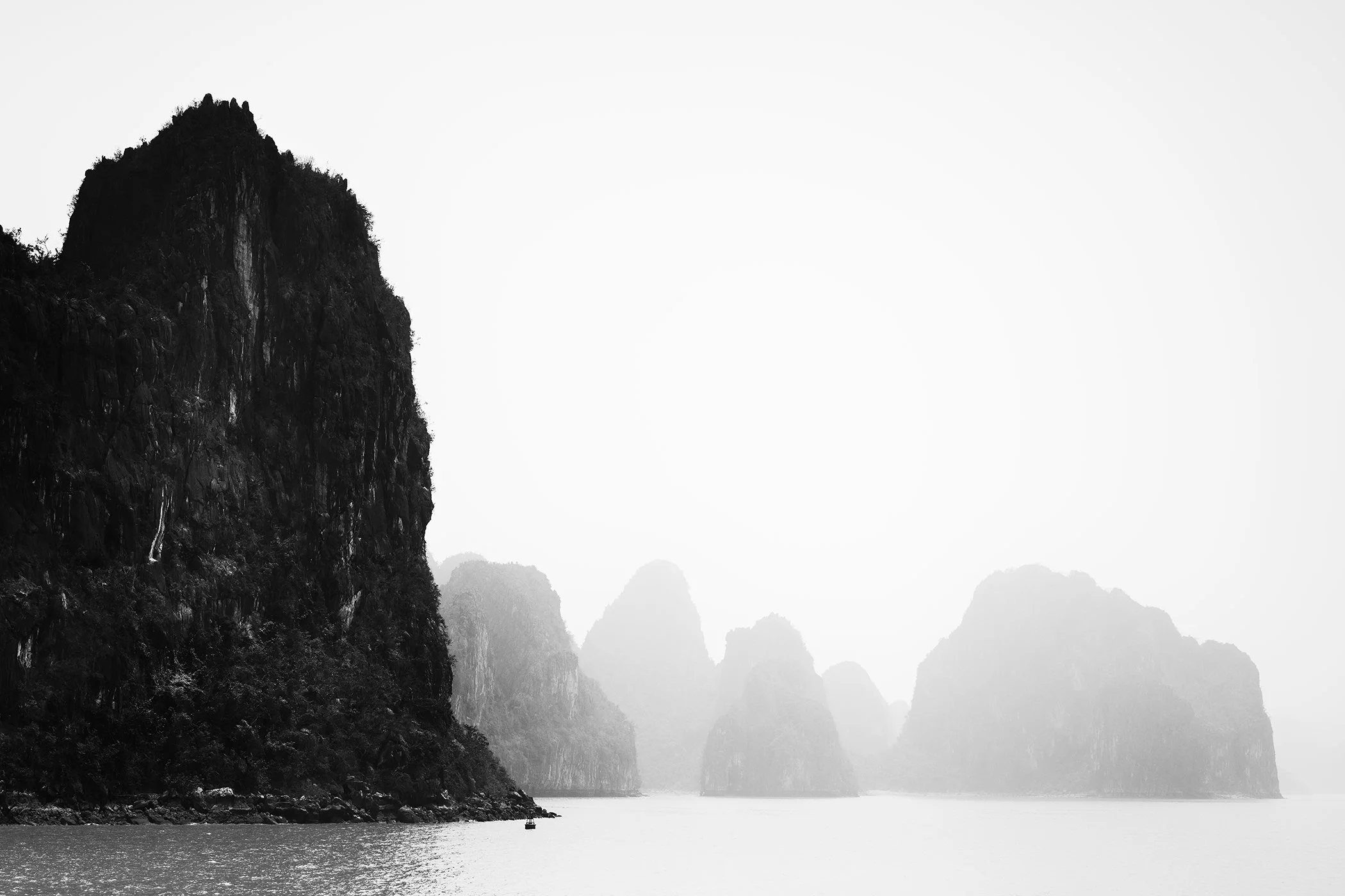Limestone karst islands rising from calm water beneath an overcast sky, with a hazy and dramatic seascape.