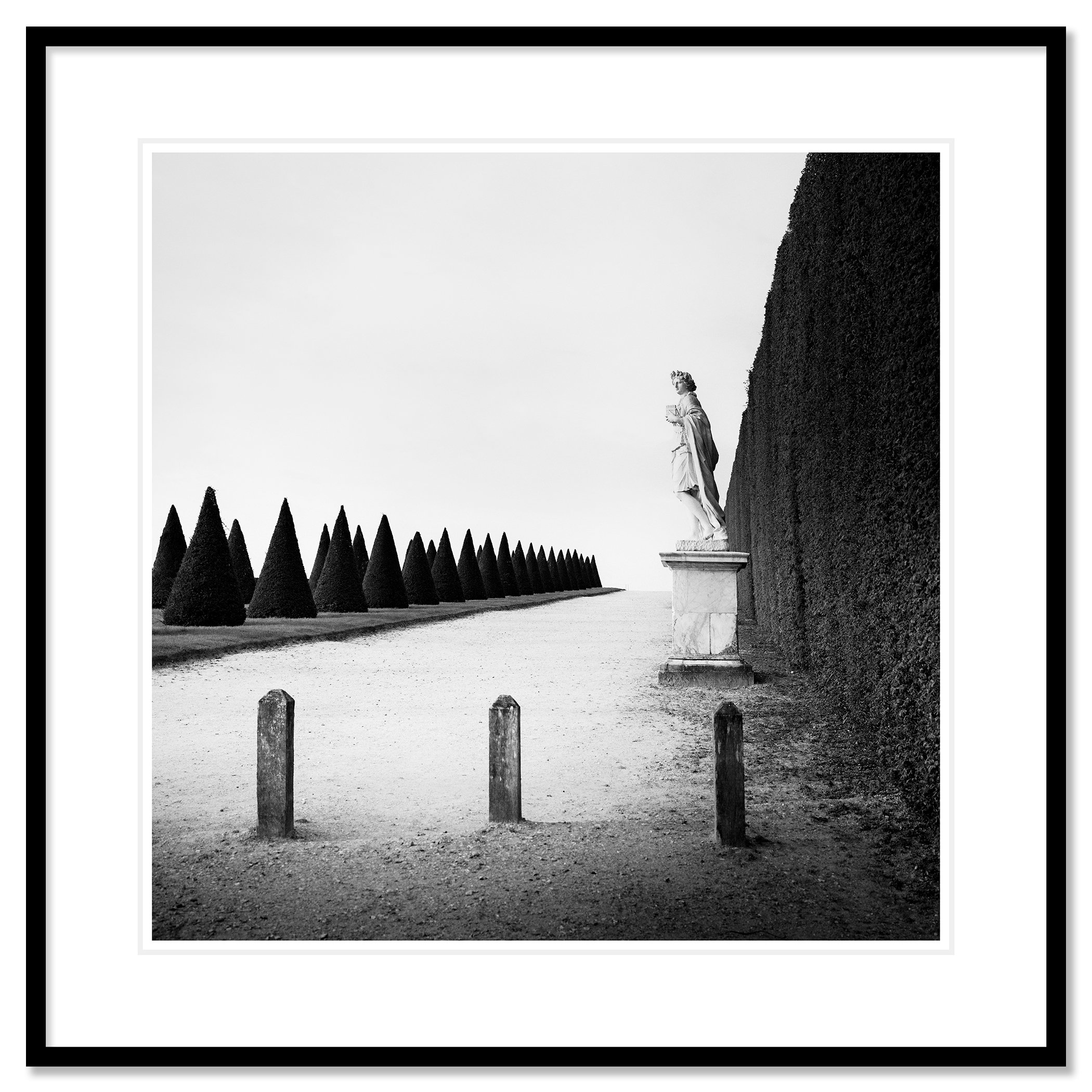 © 2017 Gerald Berghammer - Black and white landscape photography. Statue of a person along a tall hedge, with a row of trimmed cone-shaped trees. Classic framed black