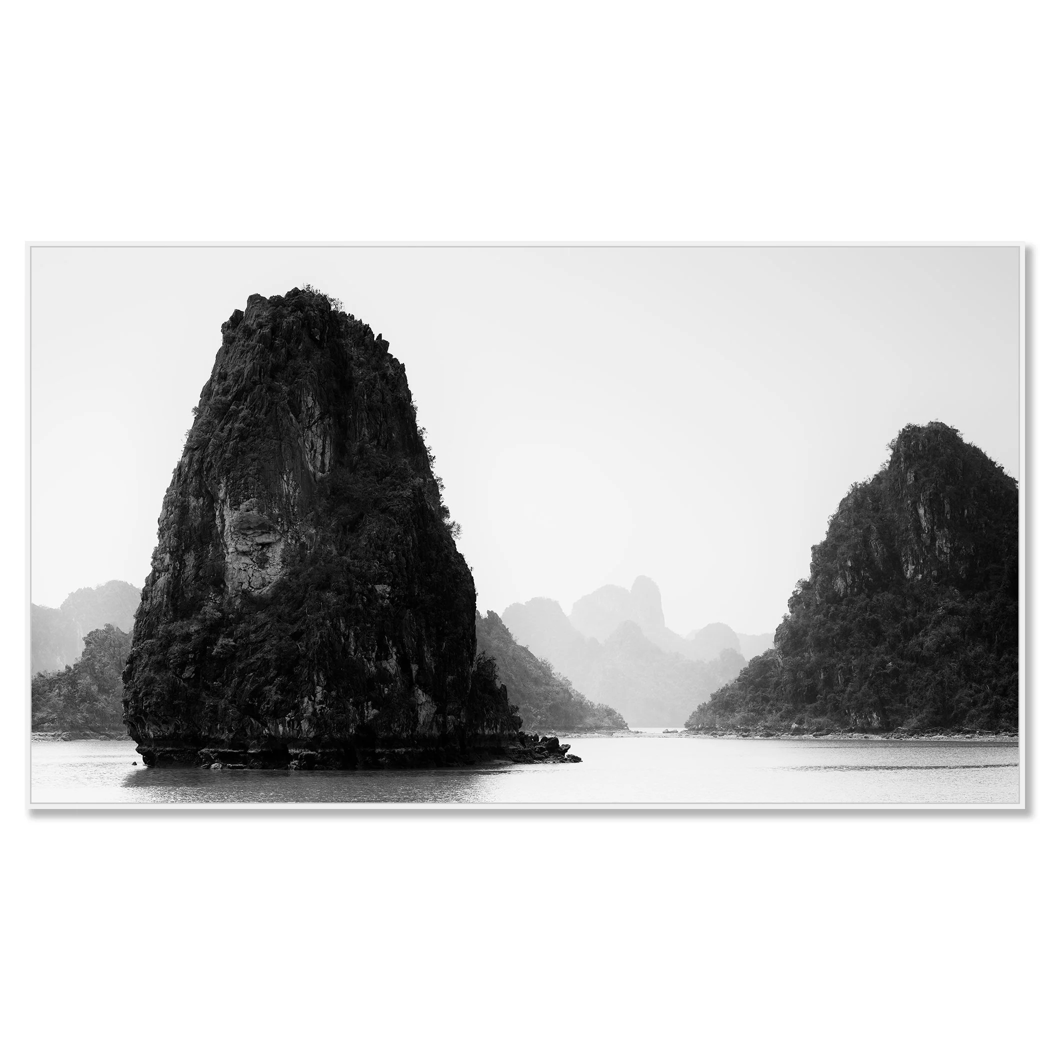 Black-and-white seascape in Vietnam showing limestone karst formations rising from calm water, with misty mountains in the background – framed ArtBox white