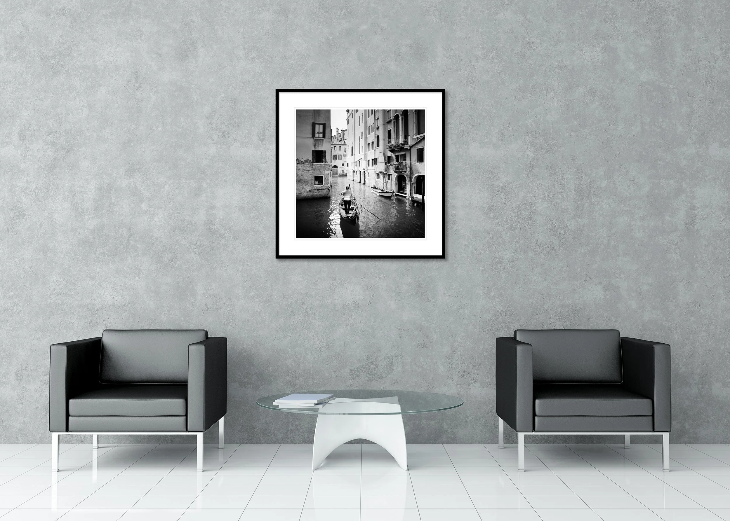 Black-and-white photo of a gondolier in a narrow Venice canal between historic buildings, archival pigment print in a classic frame with a mount.