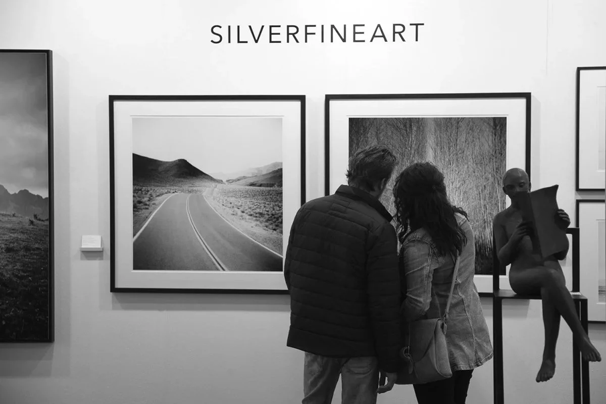 Visitors viewing framed landscape photographs by Gerald Berghammer and a figurative sculpture at art KARLSRUHE 2018.