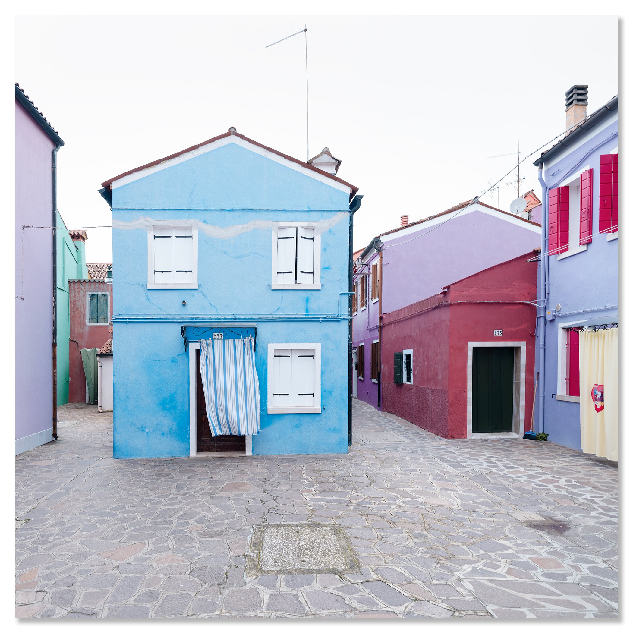 © 2025 Gerald Berghammer photo - Colorful houses in pastel shades on a cobblestone street, with colorful windows and a striped curtain hanging in front of one house. Chromaluxe frameless