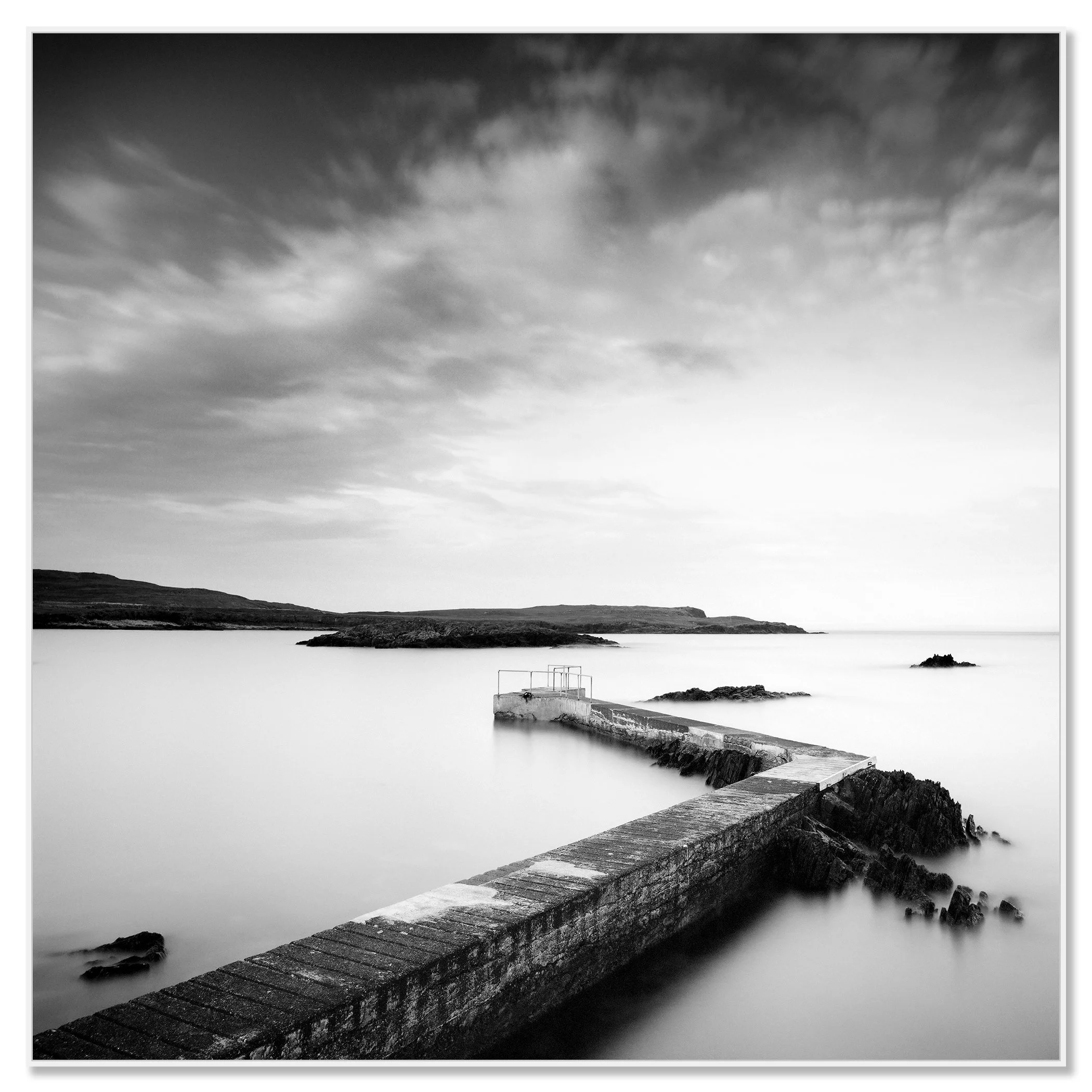 © 2014 Gerald Berghammer - Black and white seascape photography. A Concrete pier extends into calm seawater with rocky edges, under a cloudy sky. Chromaluxe framed white