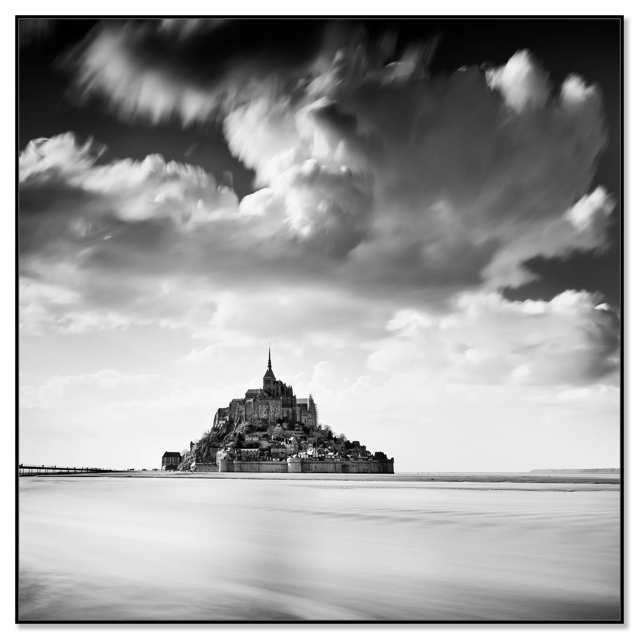 Black and white photograph of Mont Saint-Michel rising from calm tidal waters beneath dramatic clouds – framed ArtBox black