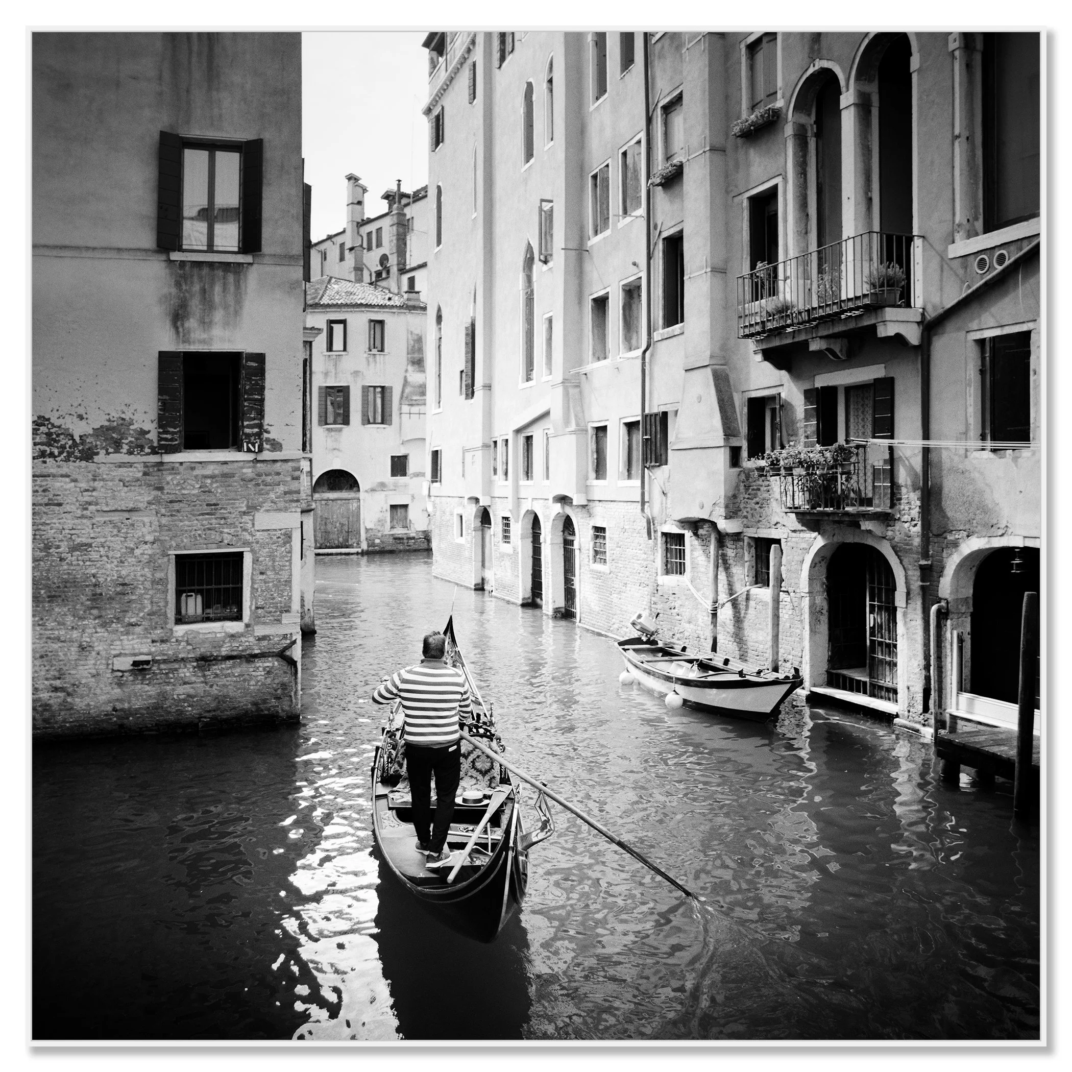 Gondolier rowing a gondola through a narrow canal in Venice, Italy, between tall historic buildings – framed ArtBox white