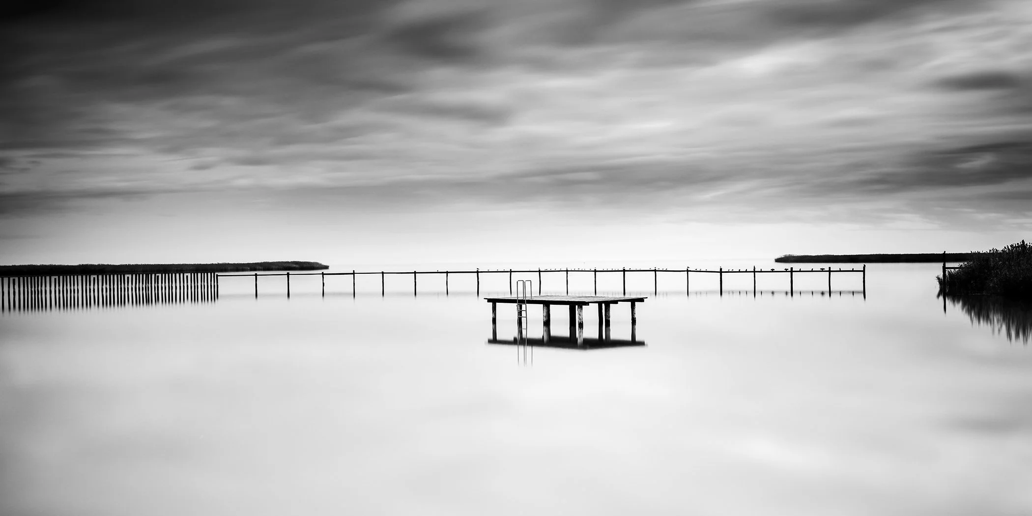 Panoramic black-and-white photograph of a wooden swimming platform on Lake Neusiedl, Austria, by Gerald Berghammer.