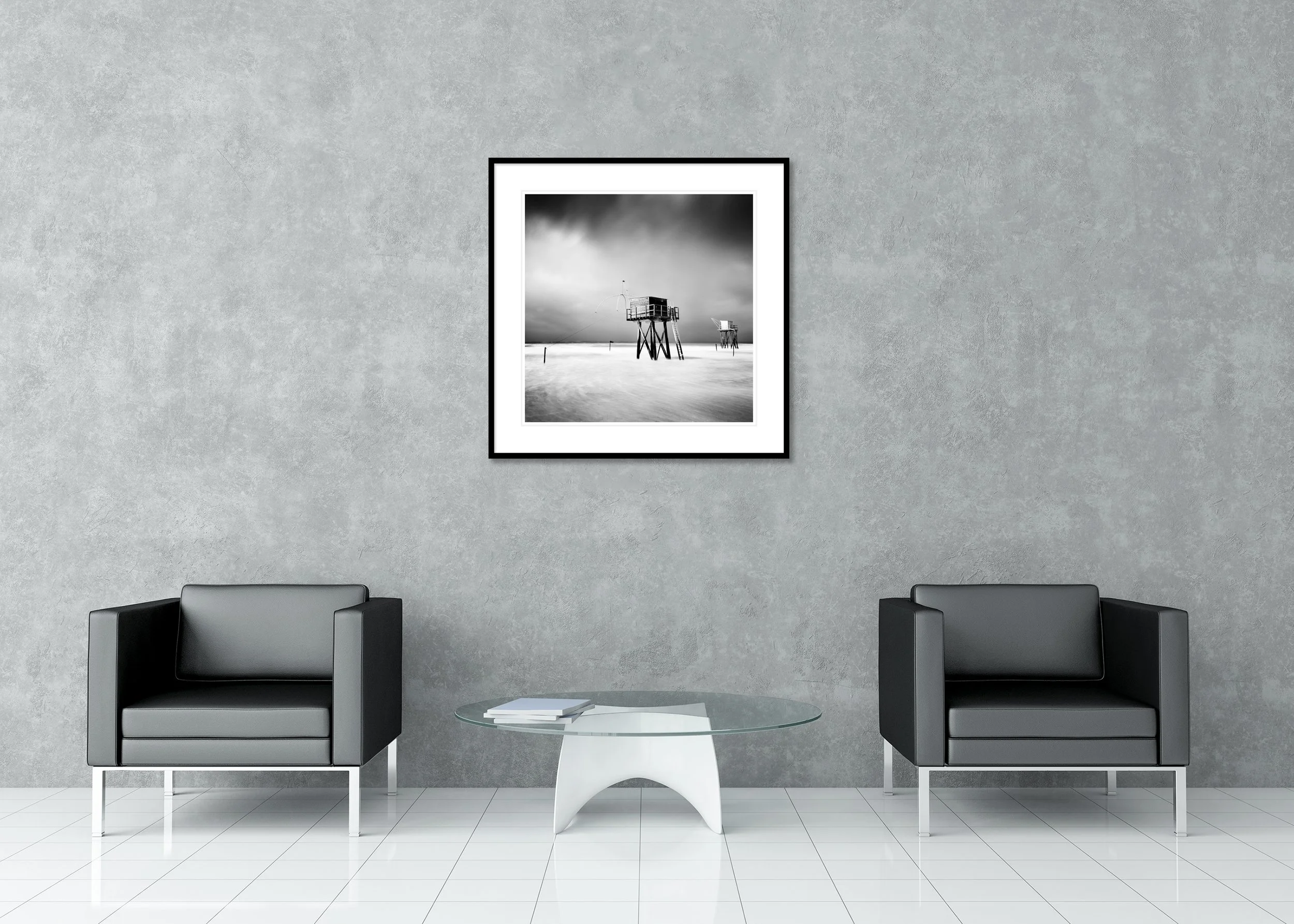 Black-and-white long-exposure photo of fishing huts on stilts at sea beneath a dramatic sky, minimalist coastal archival pigment print in a classic frame with a mount.