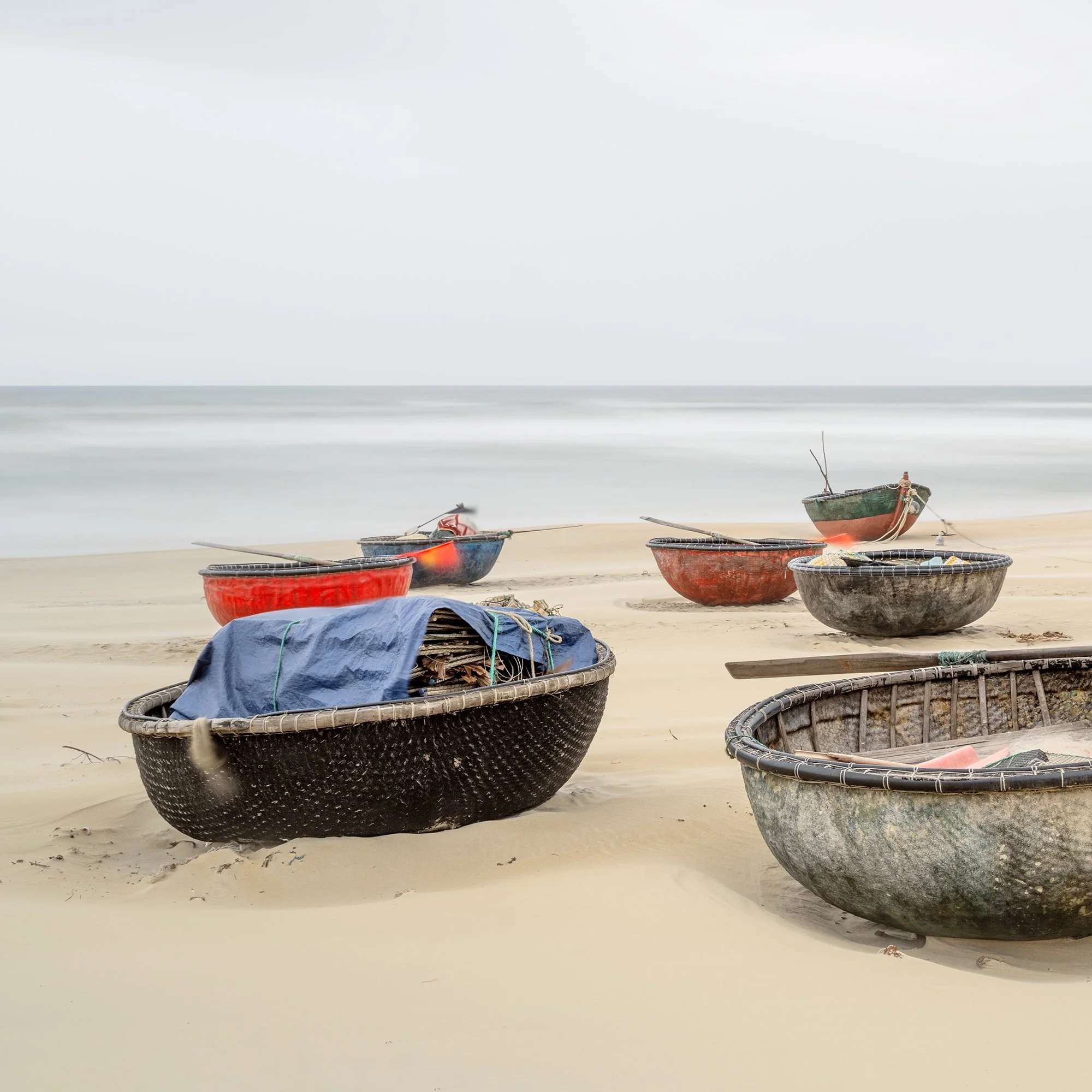Gerald Berghammer - Color landscape photography. Several small boats resting on a sandy beach with calm ocean water under an overcast sky. Print detail 1