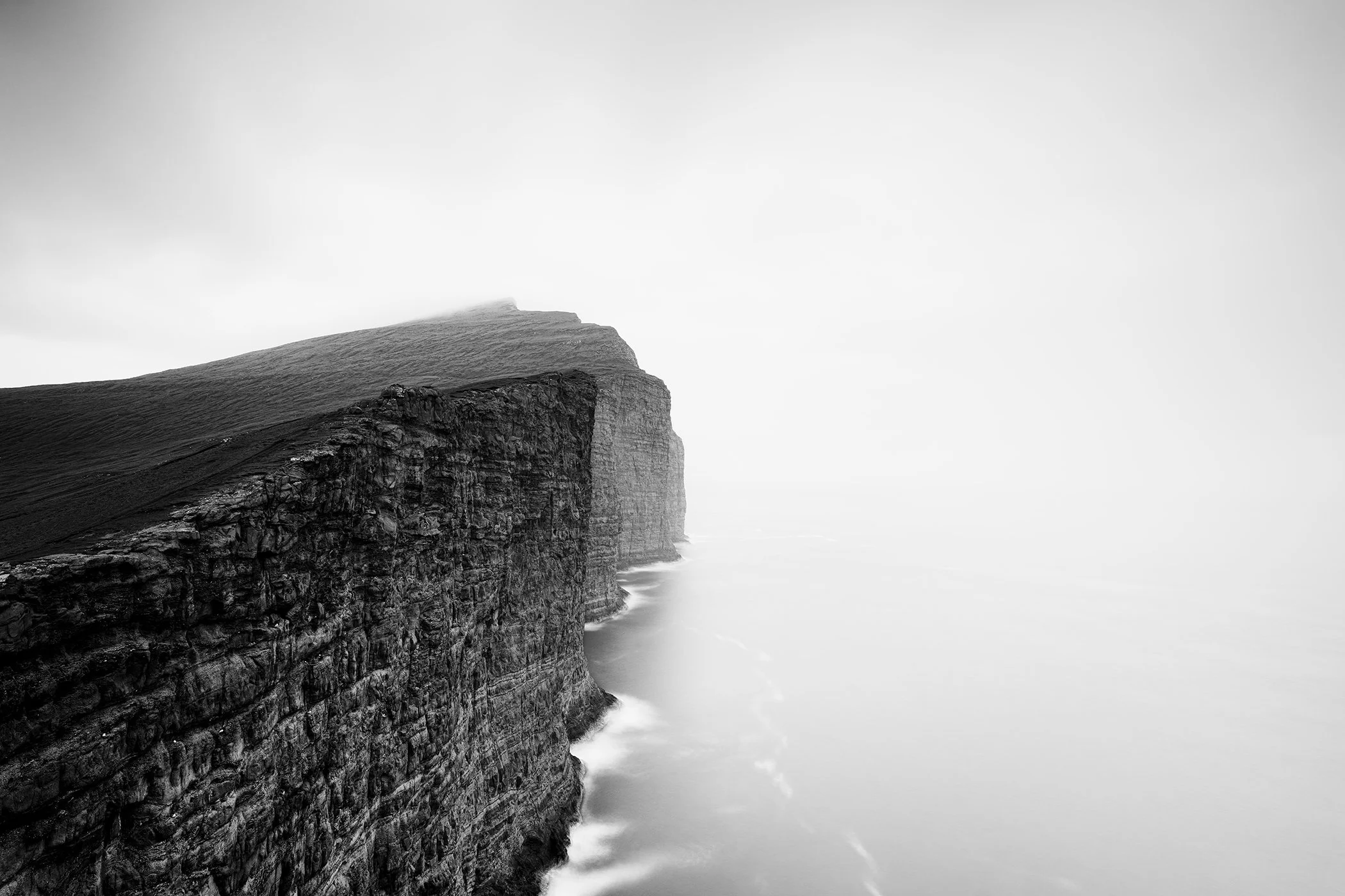 Atmospheric monochrome coastal landscape photograph by Gerald Berghammer showing rugged cliffs above a calm sea.