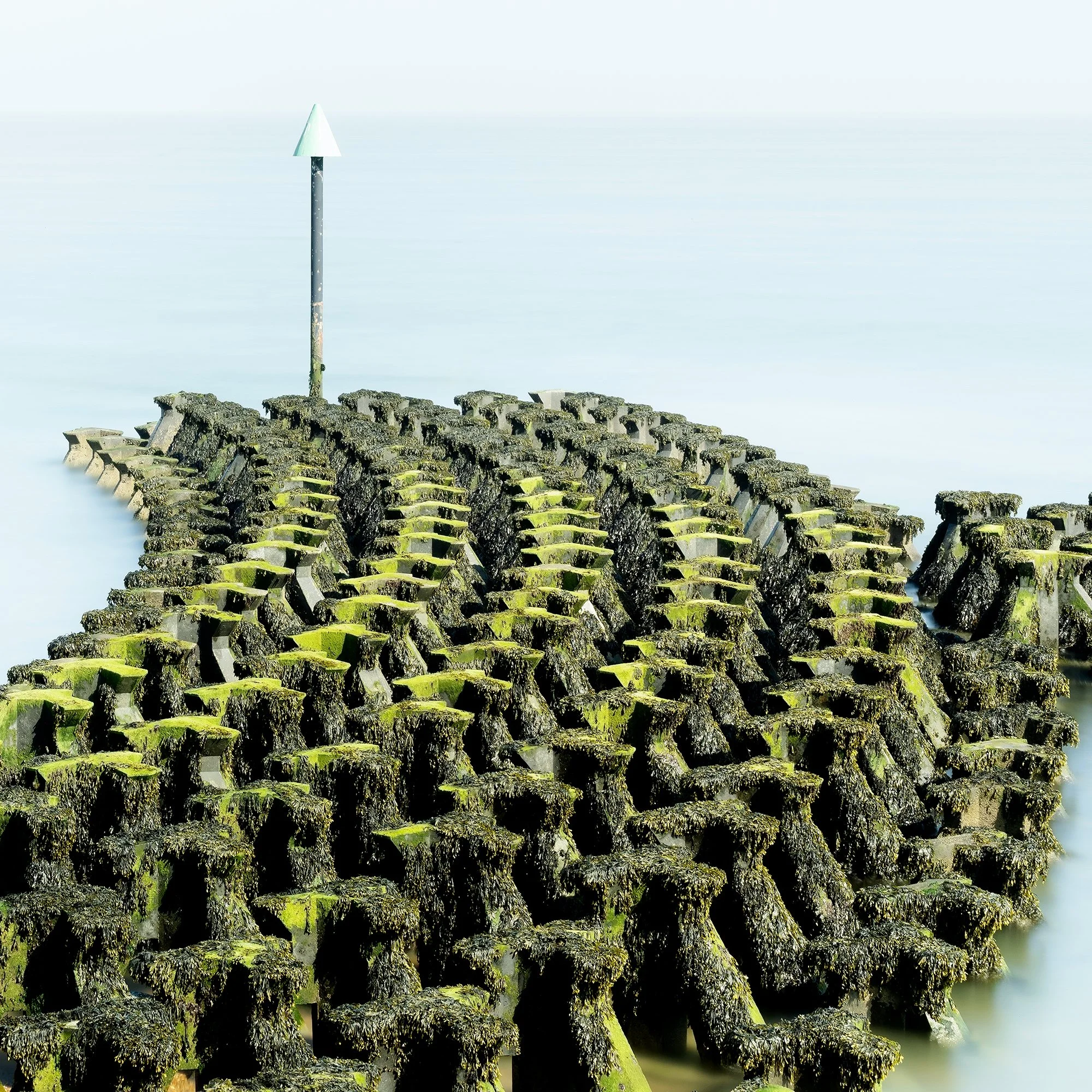 Gerald Berghammer - Color seascape panorama photography. Concrete breakwater structures on a beach extending into the water, with a pole at the end. Print detail 3