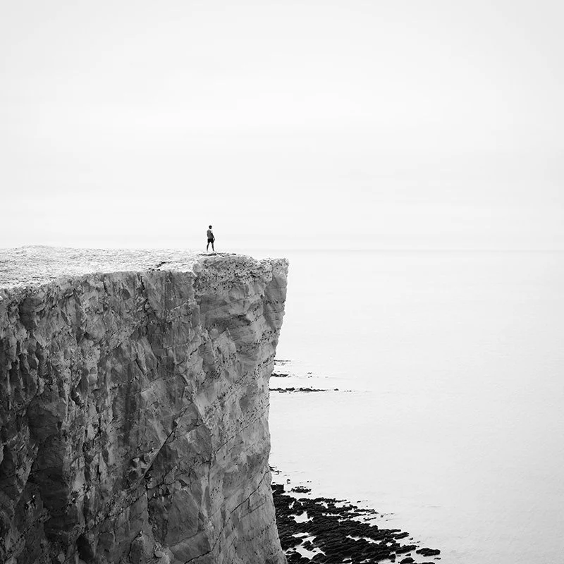 Top of the Cliffs Study 1 by Gerald Berghammer, minimalist black-and-white photograph of a solitary figure standing on high coastal cliffs in England.