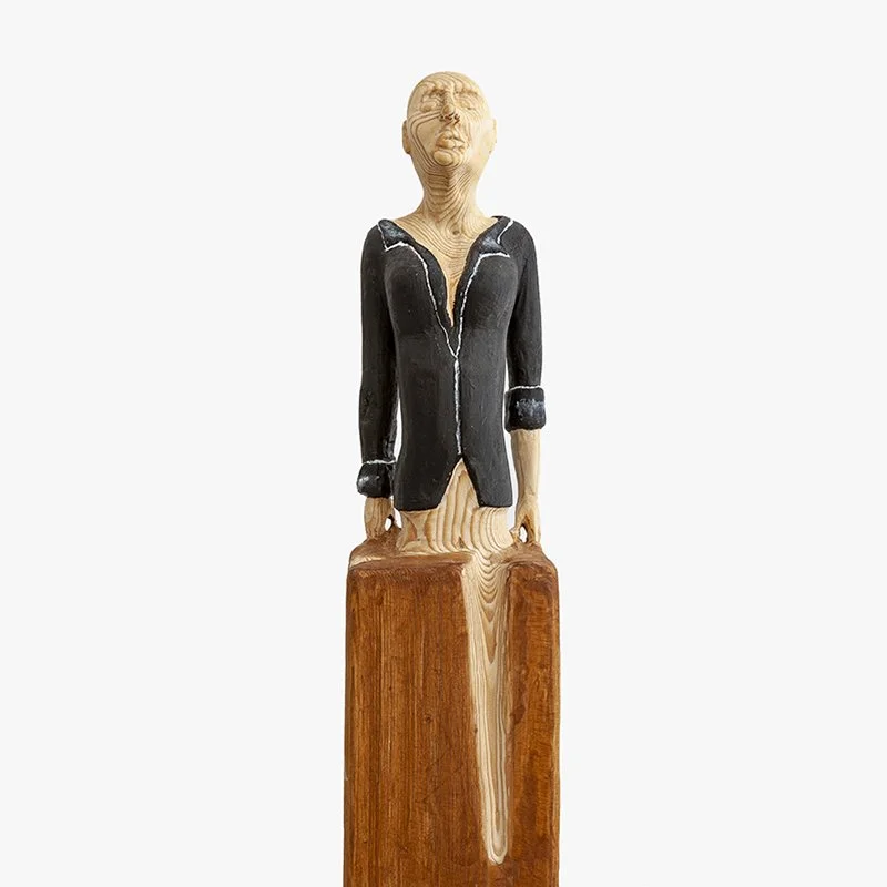 Wooden sculpture of a woman with short hair, black jacket and suitcase by Austrian artist ToPu – Thomas Pusswald.