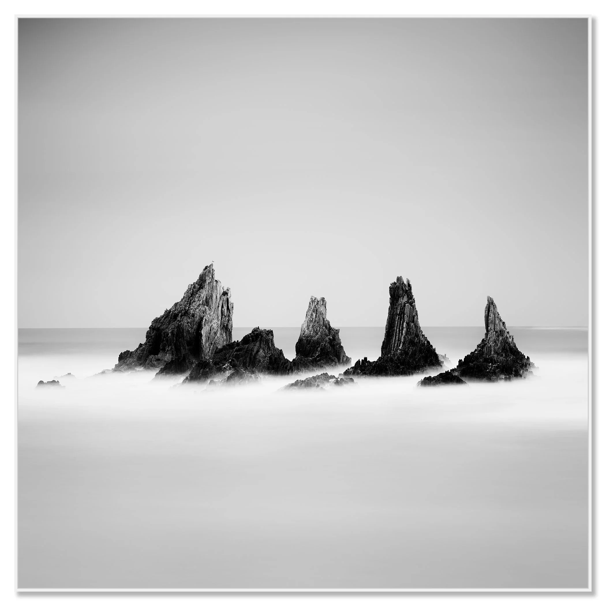 Black and white photograph of five jagged sea stacks rising from the Atlantic Ocean, with calm water and a clear sky – framed ArtBox white