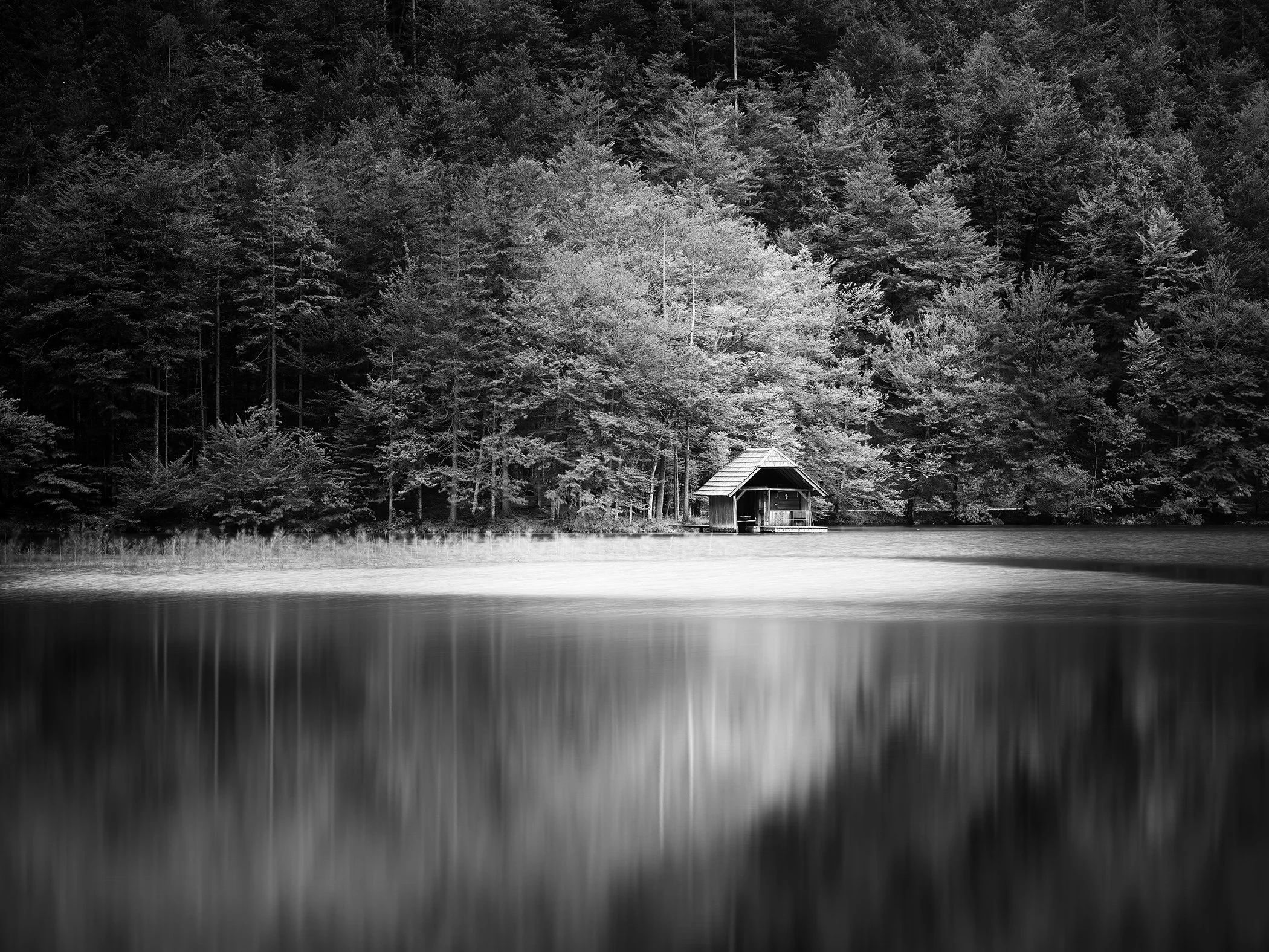 Black-and-white long-exposure photograph of a wooden boathouse beside Langbathsee, Austria, by Gerald Berghammer.