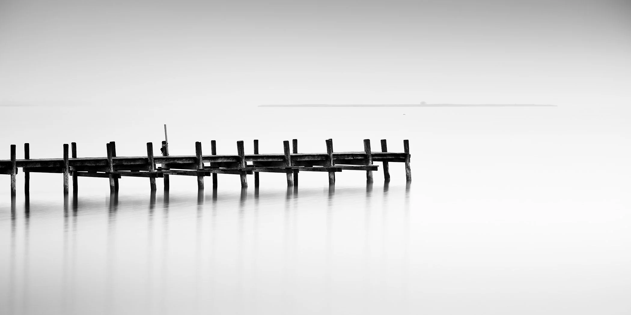 Black-and-white fine art photograph of a quiet wooden dock extending over calm water in Austria.