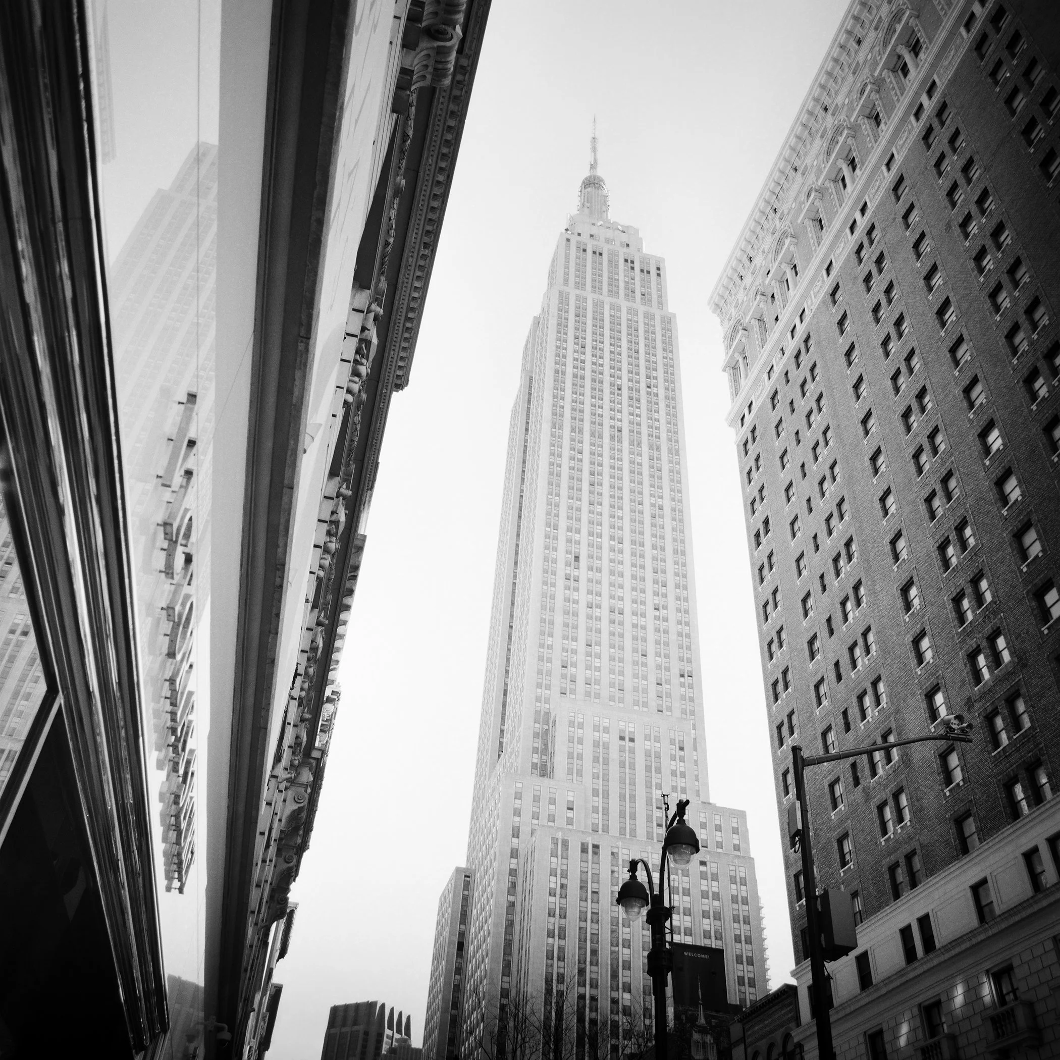 Empire State Building seen from street level between Manhattan skyscrapers, black-and-white photograph by Gerald Berghammer