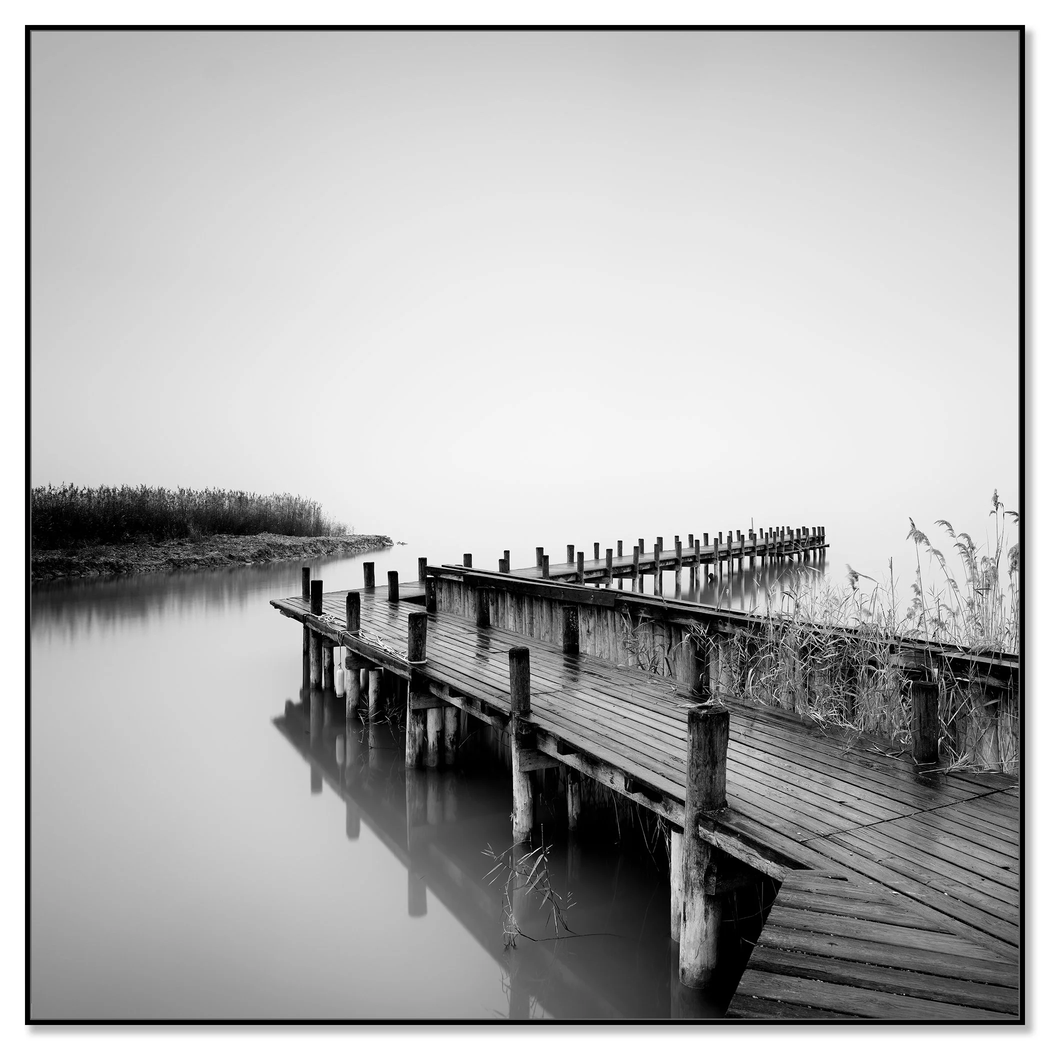 Minimalist black and white wall art showing a wooden jetty on still water with reeds at the edge – framed ArtBox black