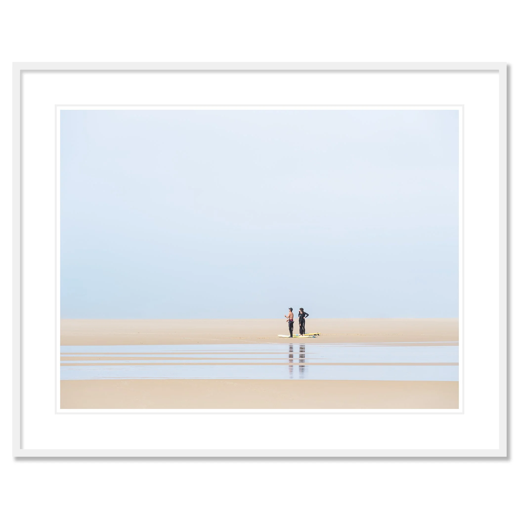 Gerald Berghammer - Color landscape Photography. People stand on a sandy beach near the ocean, wearing wetsuits and surfboards against a pale blue sky. Classic framed white