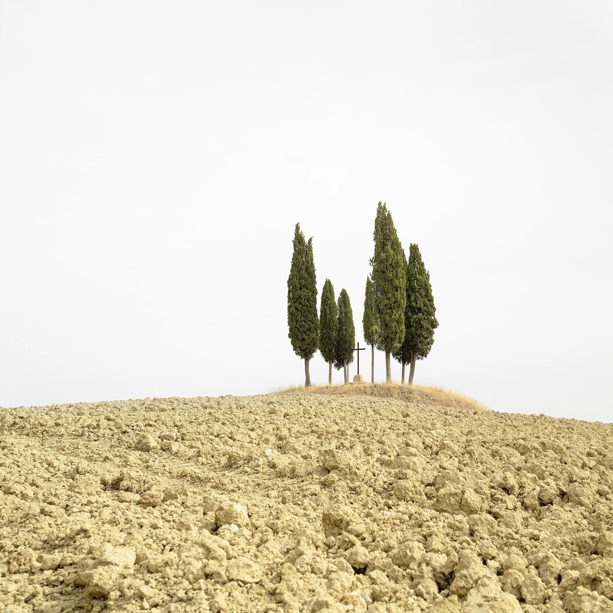 Cypress Tree on a Hill with a Cross, minimalist colour landscape photograph of cypress trees and a cross on a Tuscan hillside by Gerald Berghammer.