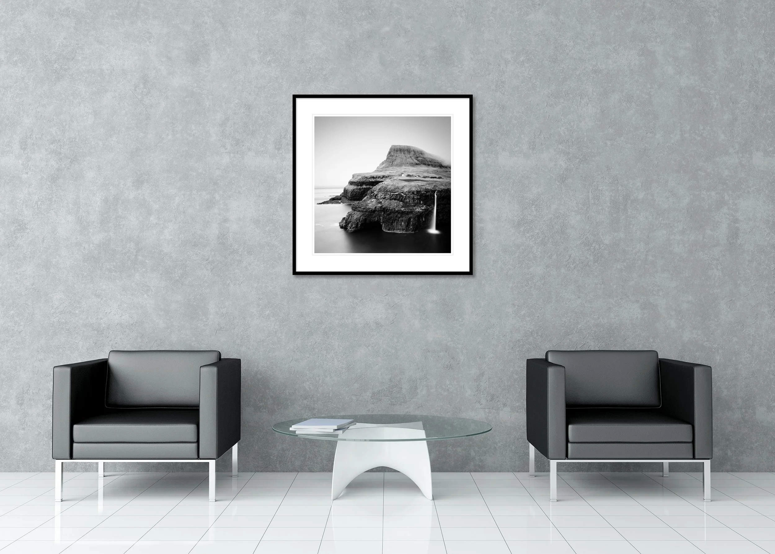Black-and-white archival pigment print of a Faroe Islands coastal cliff with waterfall flowing into the ocean near a remote village, in a classic frame with mount.