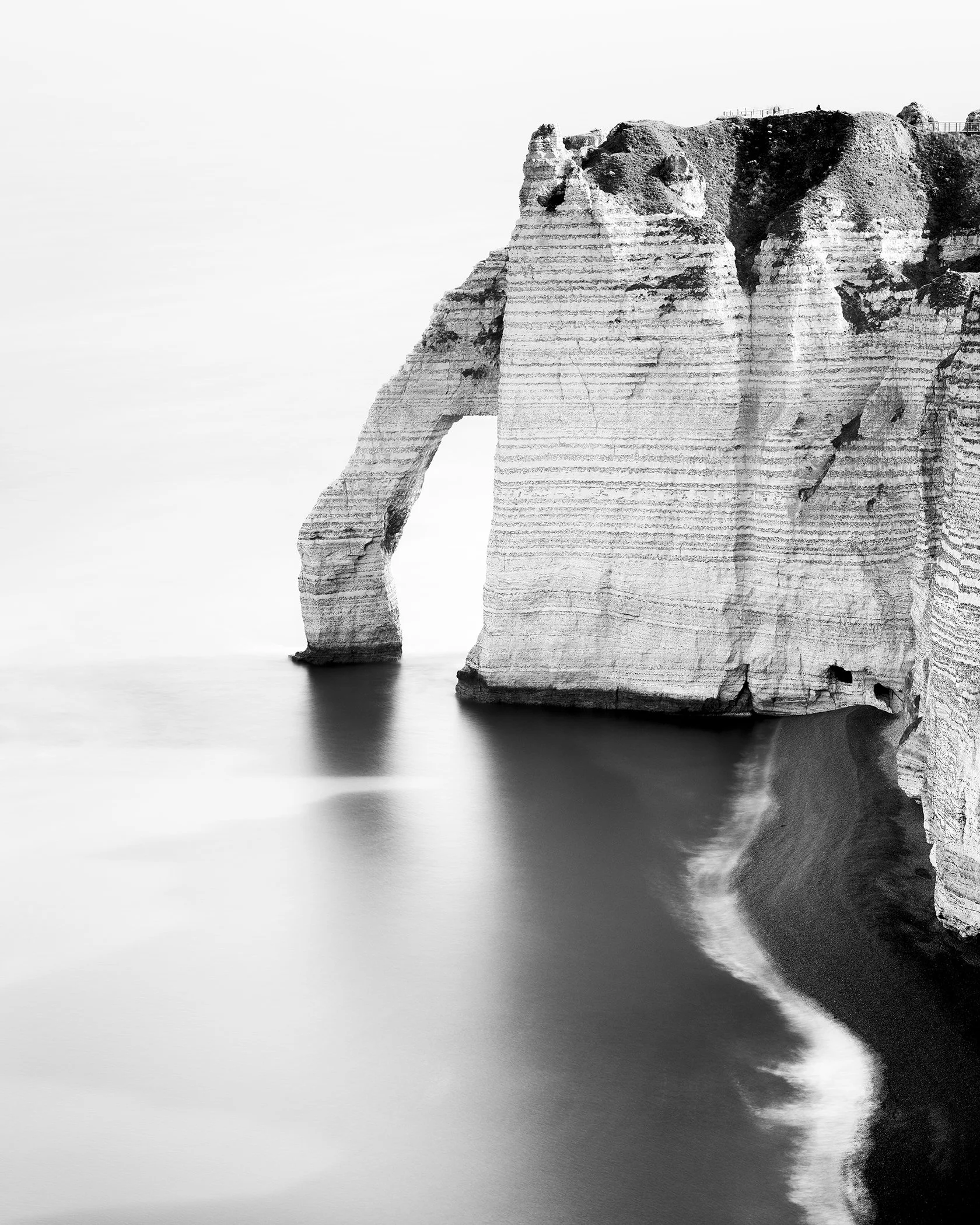 Black-and-white long-exposure photograph of Étretat’s chalk cliffs and sea arch in Normandy, France. Photo by Gerald Berghammer.