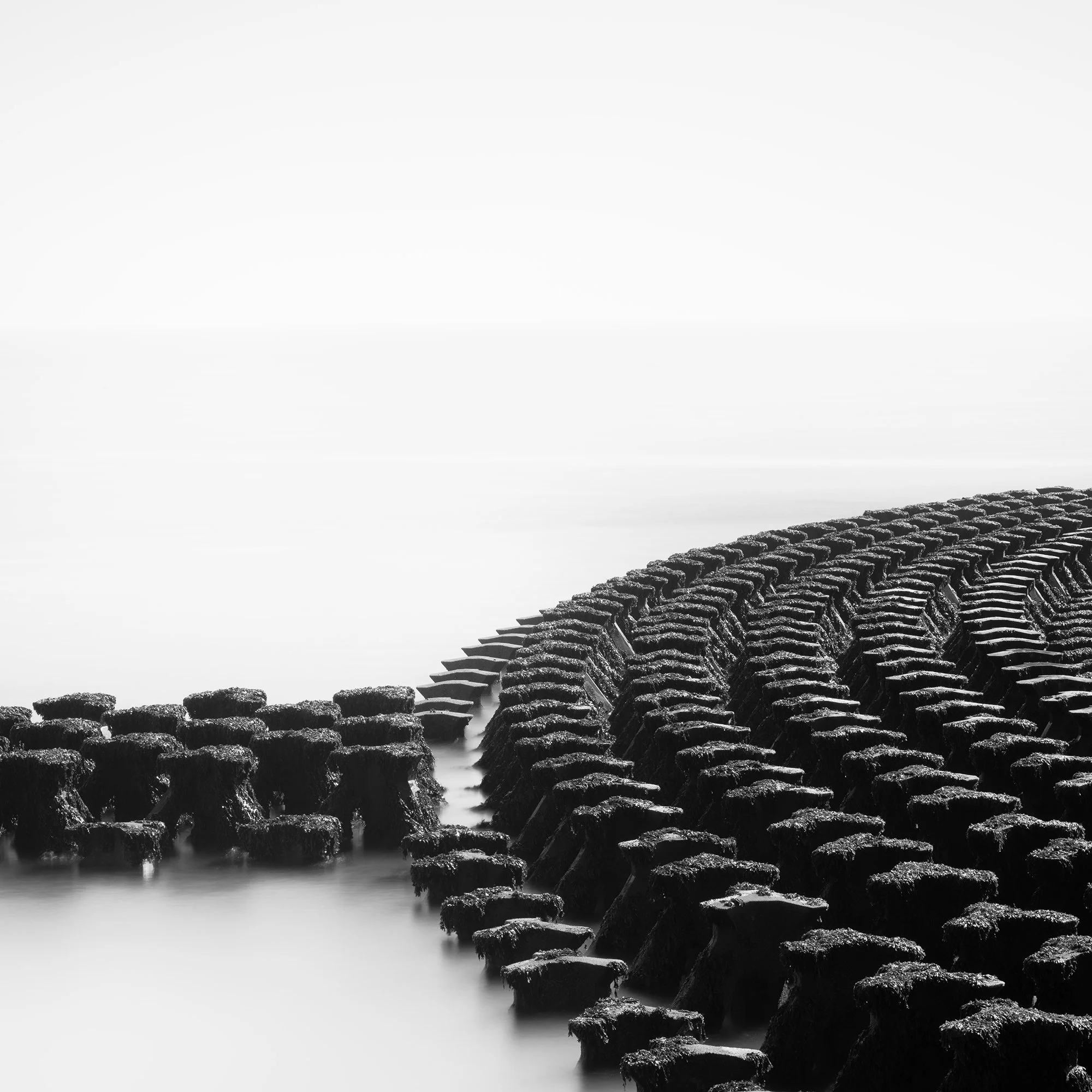 Gerald Berghammer - Black and white minimalist photography. A curved stone jetty extending into a calm body of water, with a tall navigation marker at the end. Print detail 1