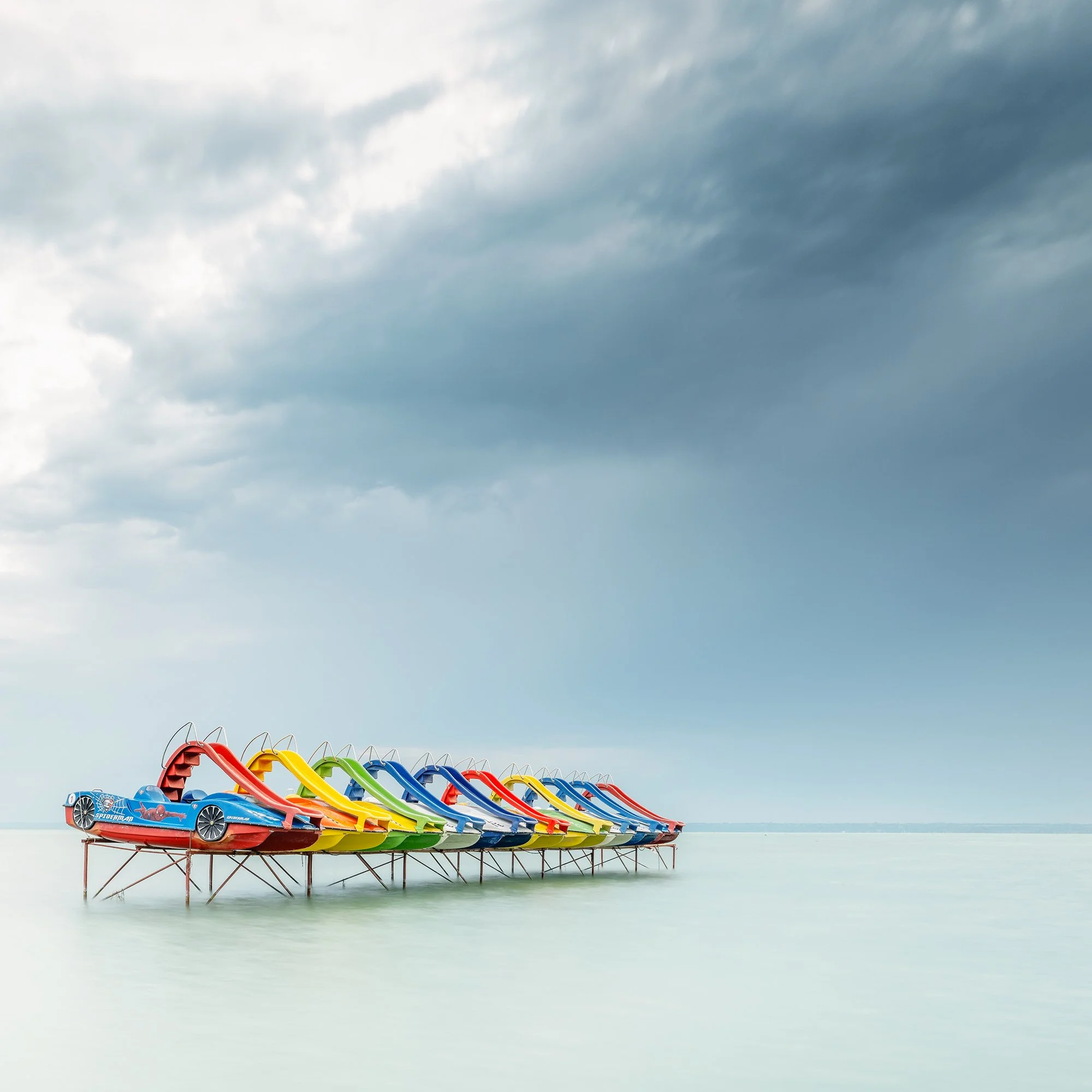 © 2021 Gerald Berghammer - Color panorama waterscape photography. A row of colorful pedal boats on the lake Balaton with dramatic cloudy sky. Print detail 2