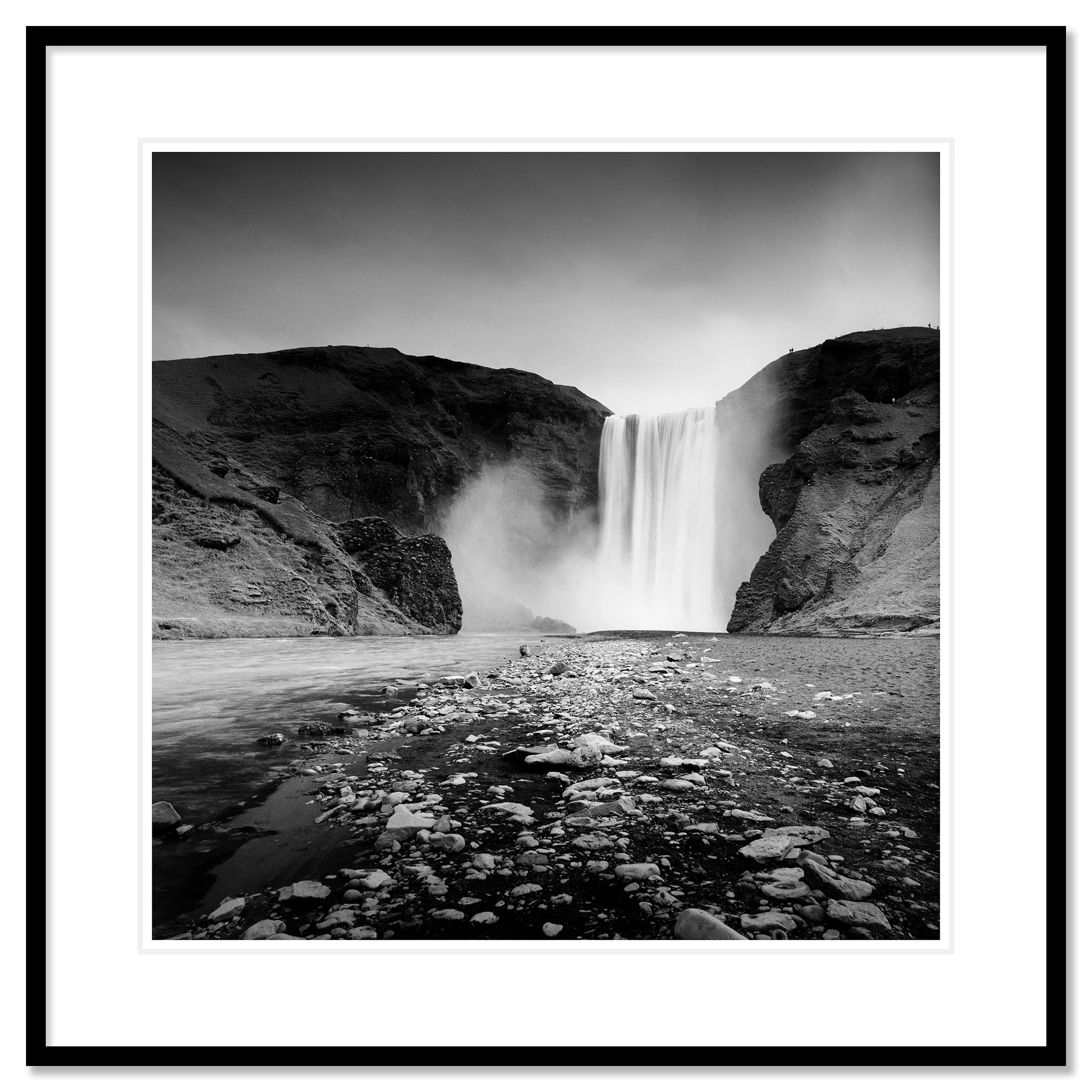 Gerald Berghammer - Black and white long exposure waterscape photography. A large waterfall flowing between rugged cliffs into a rocky river. Classic framed black