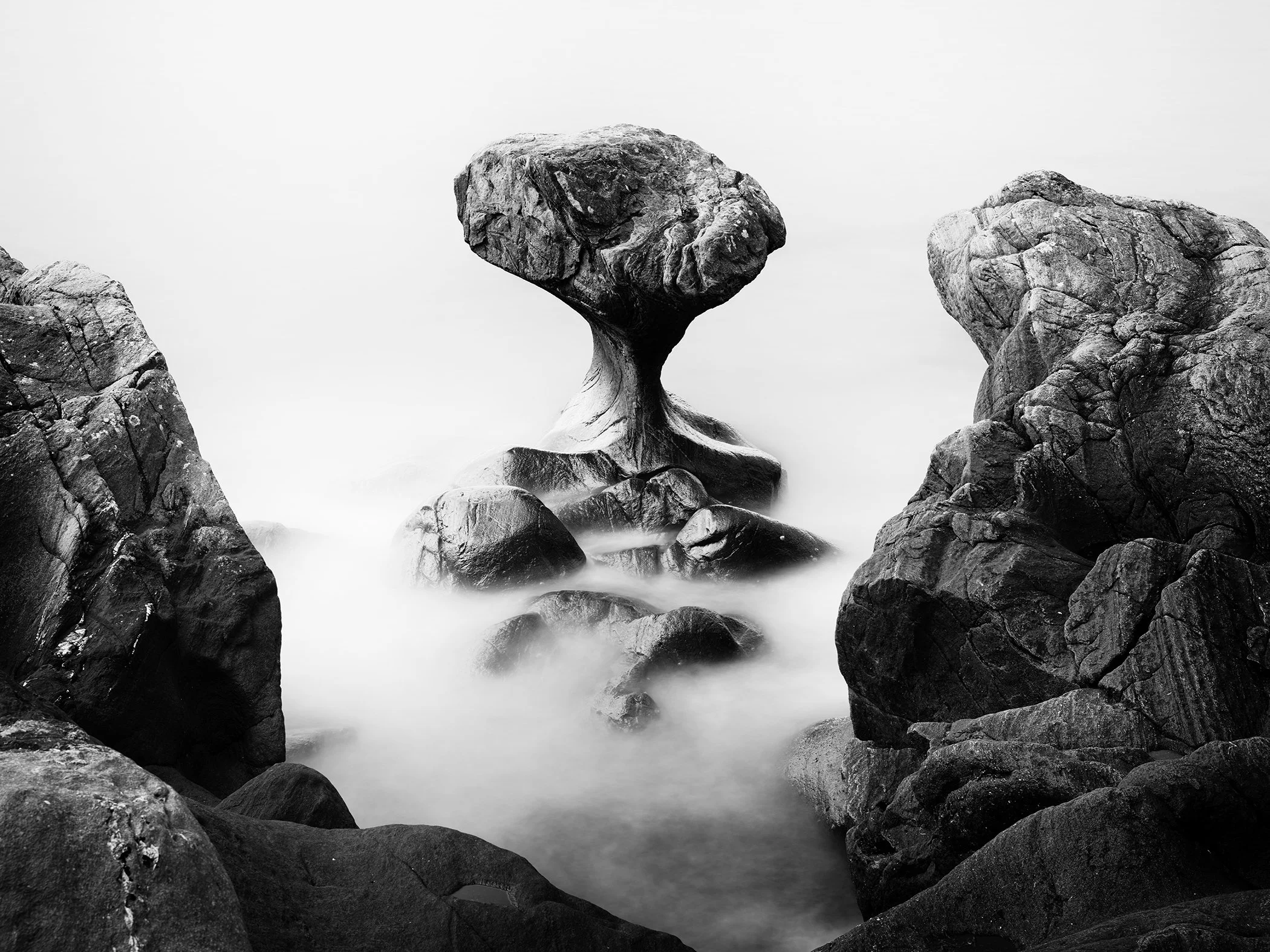 Large rock balanced on a smaller stone in water, forming a natural mushroom-like structure.
