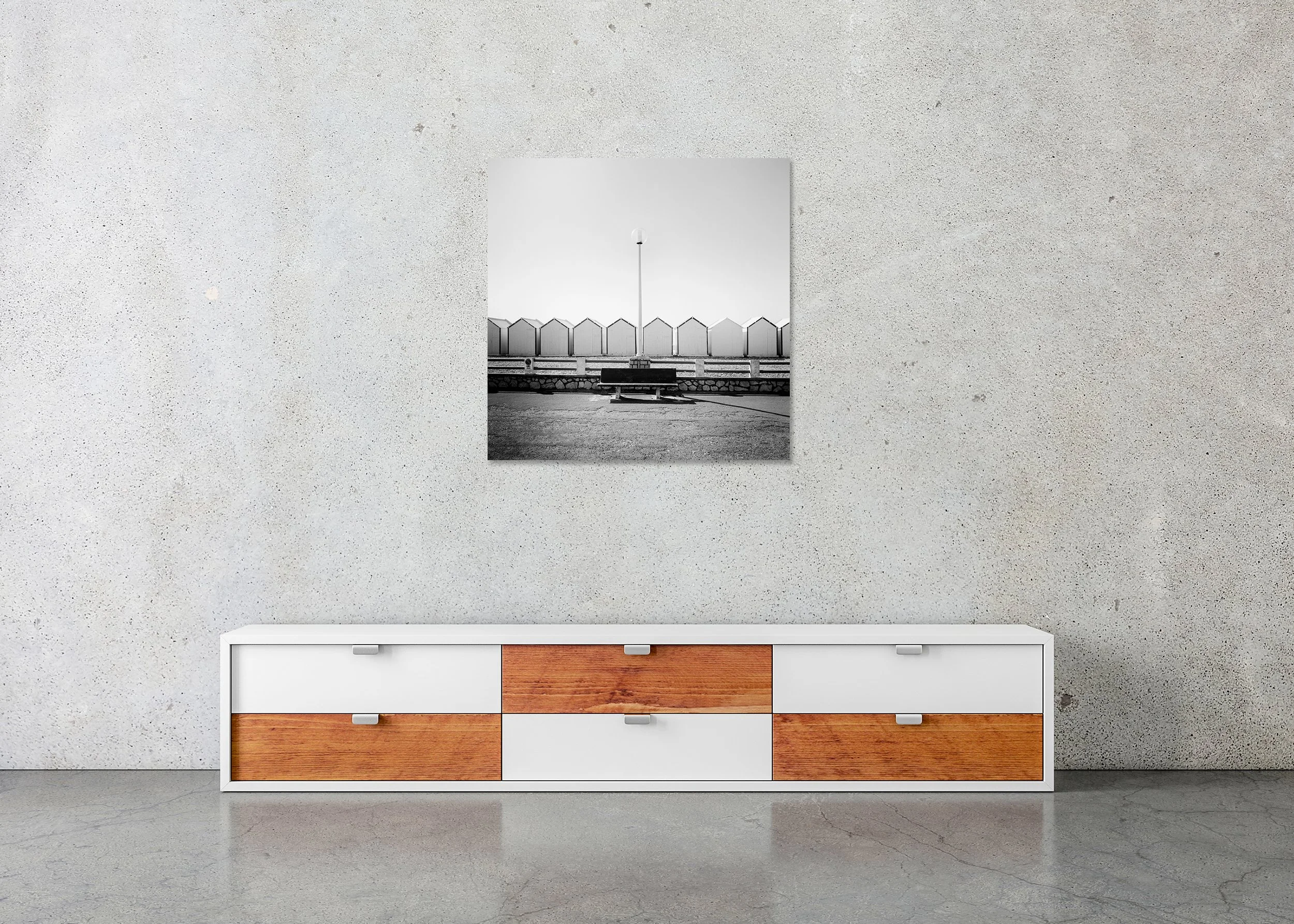 Black-and-white coastal photograph in France with an empty bench and centred streetlamp in front of geometric beach huts, ChromaLuxe metal print, frameless.