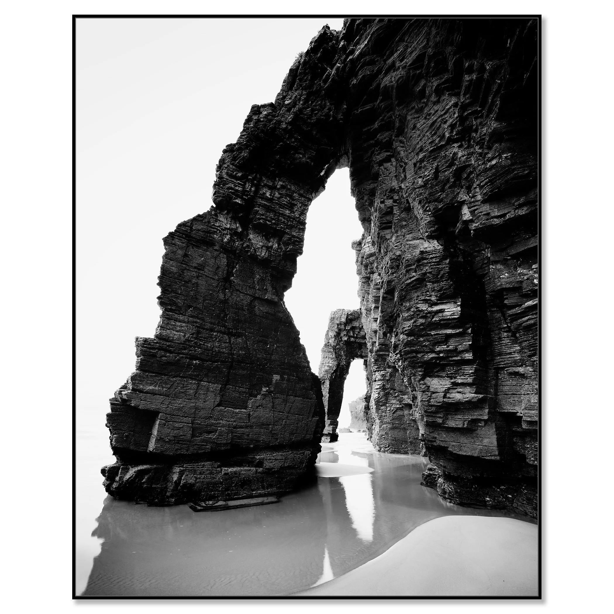Black and white long-exposure minimalist seascape of rock arches on a beach with wet sand reflections – framed ArtBox black