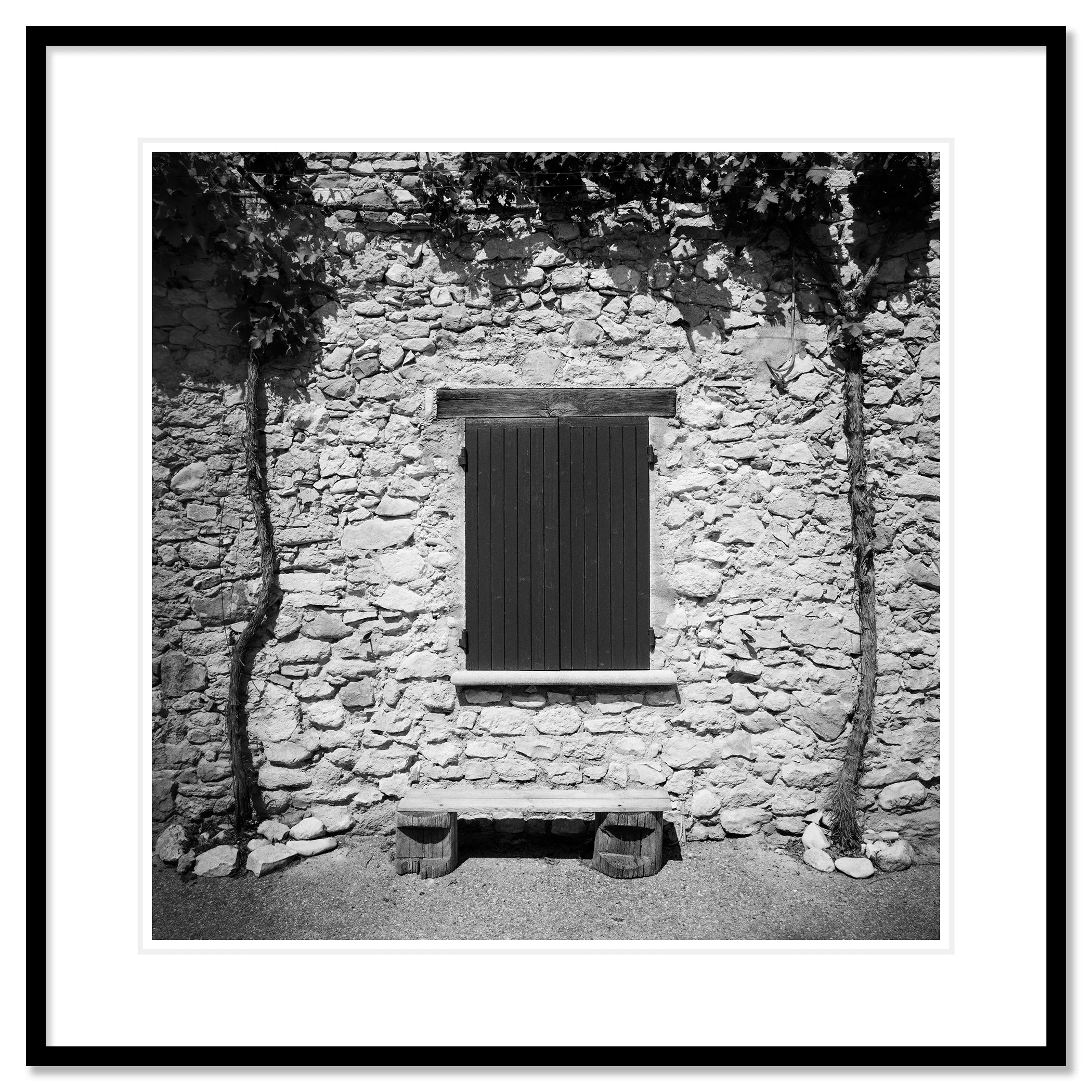 Gerald Berghammer - Black & white photography. Stone wall with a closed wooden window shutter, flanked by climbing vines on both sides, and a small bench. Classic framed black