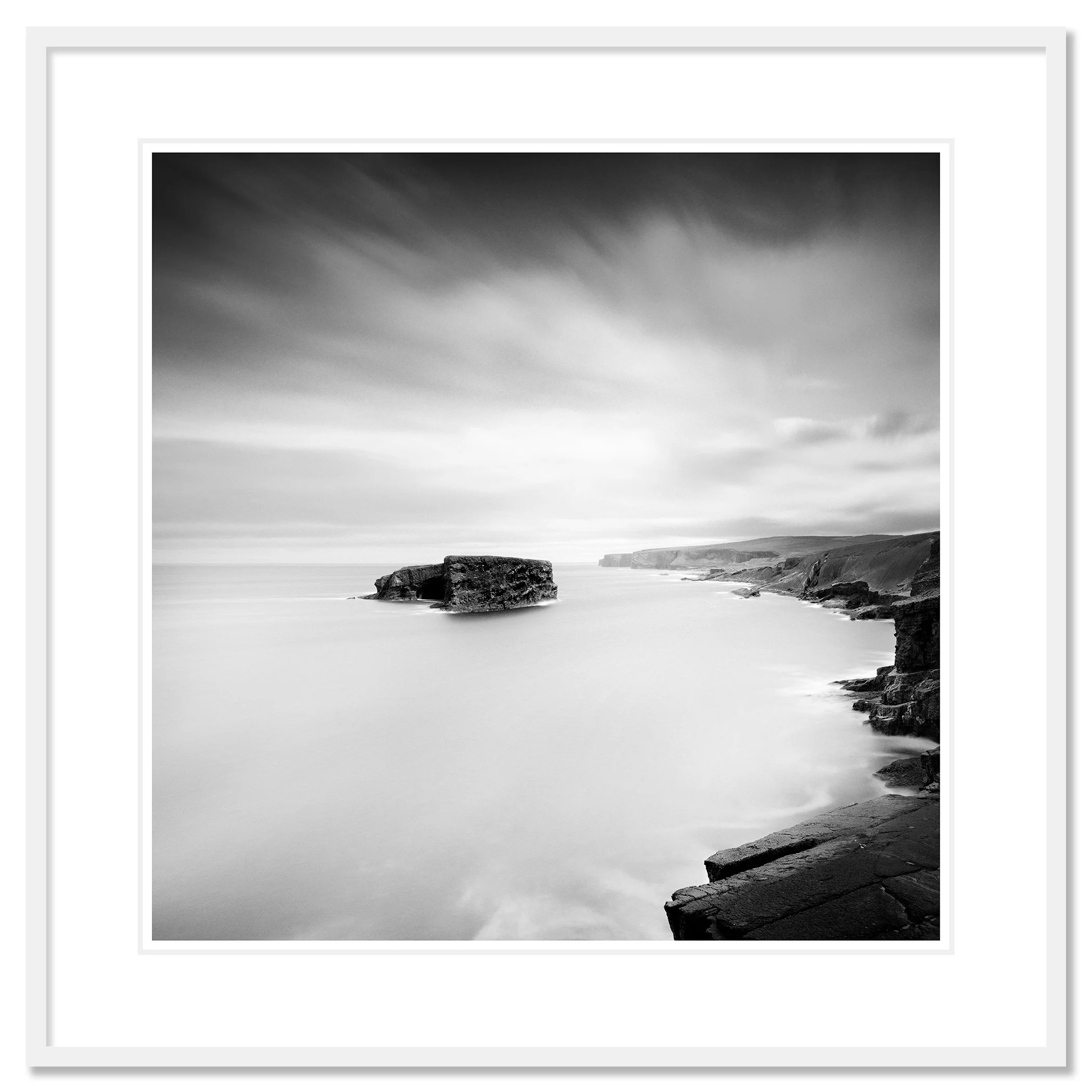 Gerald Berghammer - Black and white long exposure seascape photography. Rocky coastal landscape with cliffs and a large rock formation in the ocean. Classic framed white