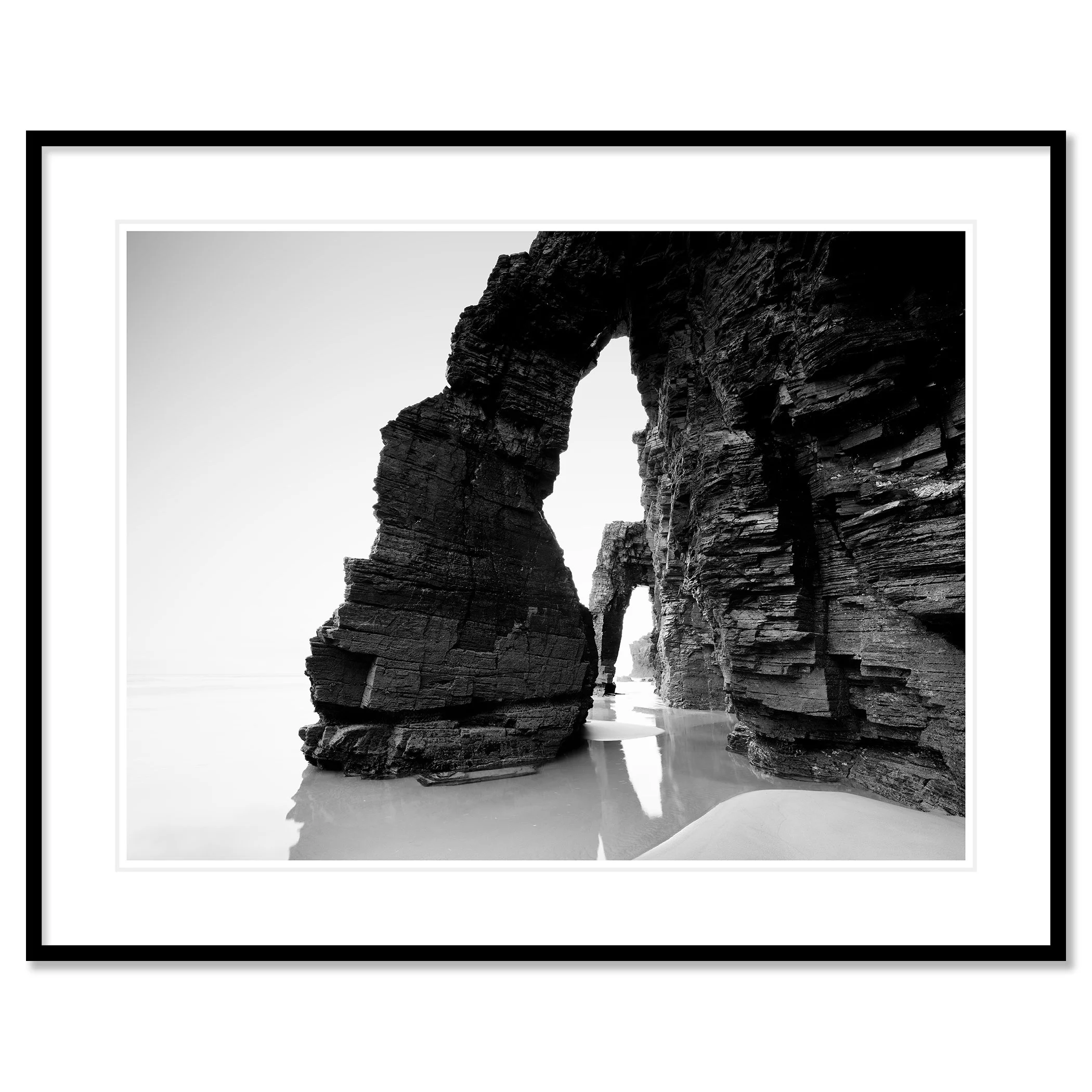 Gerald Berghammer - Black and white beach seascape photography. Large natural rock arch formations on a beach with water reflecting the rocks. Classic framed black