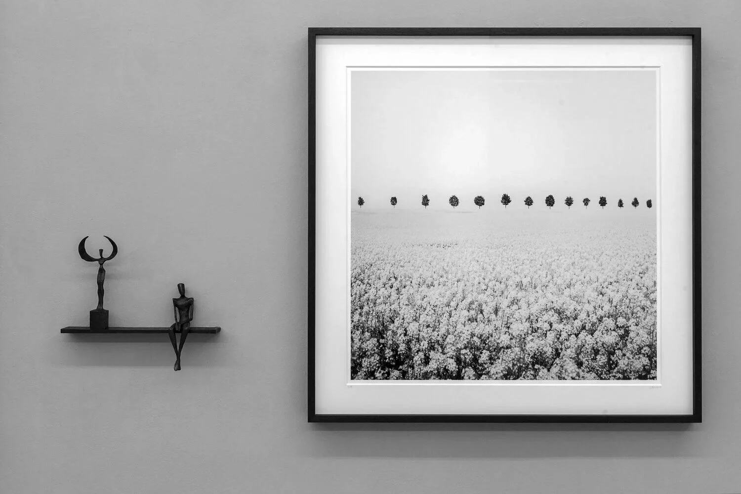 Framed black-and-white photograph of a tree-lined field by Gerald Berghammer, displayed beside two sculptures.