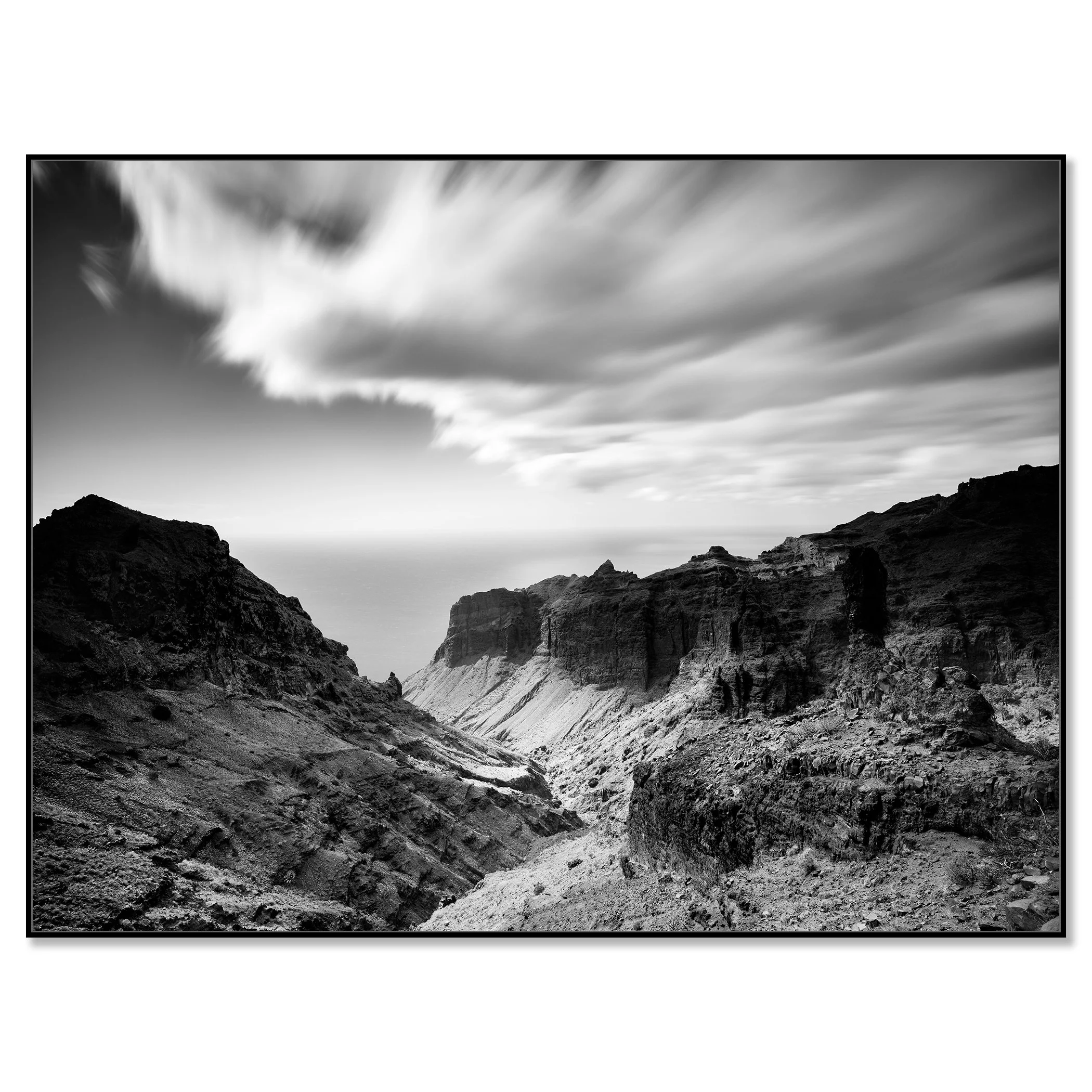 Deep canyon with rugged rock formations and towering cliffs under a sky with clouds drifting overhead – framed ArtBox black