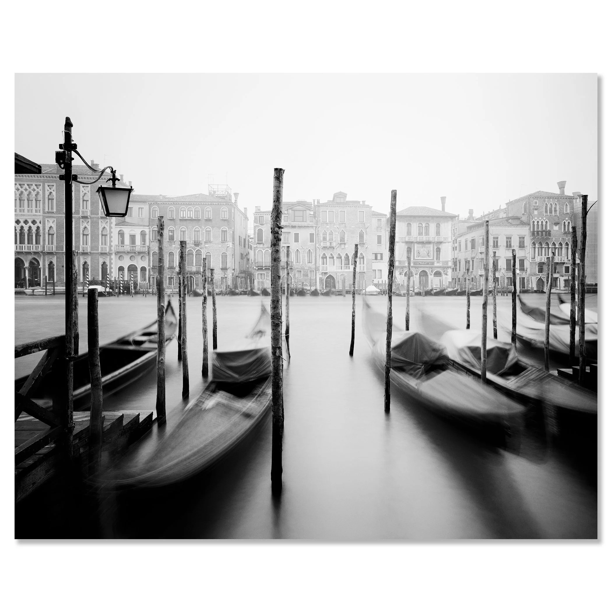 Black and white long-exposure photo of gondolas on a quiet Venice canal with wooden poles, dibond frameless