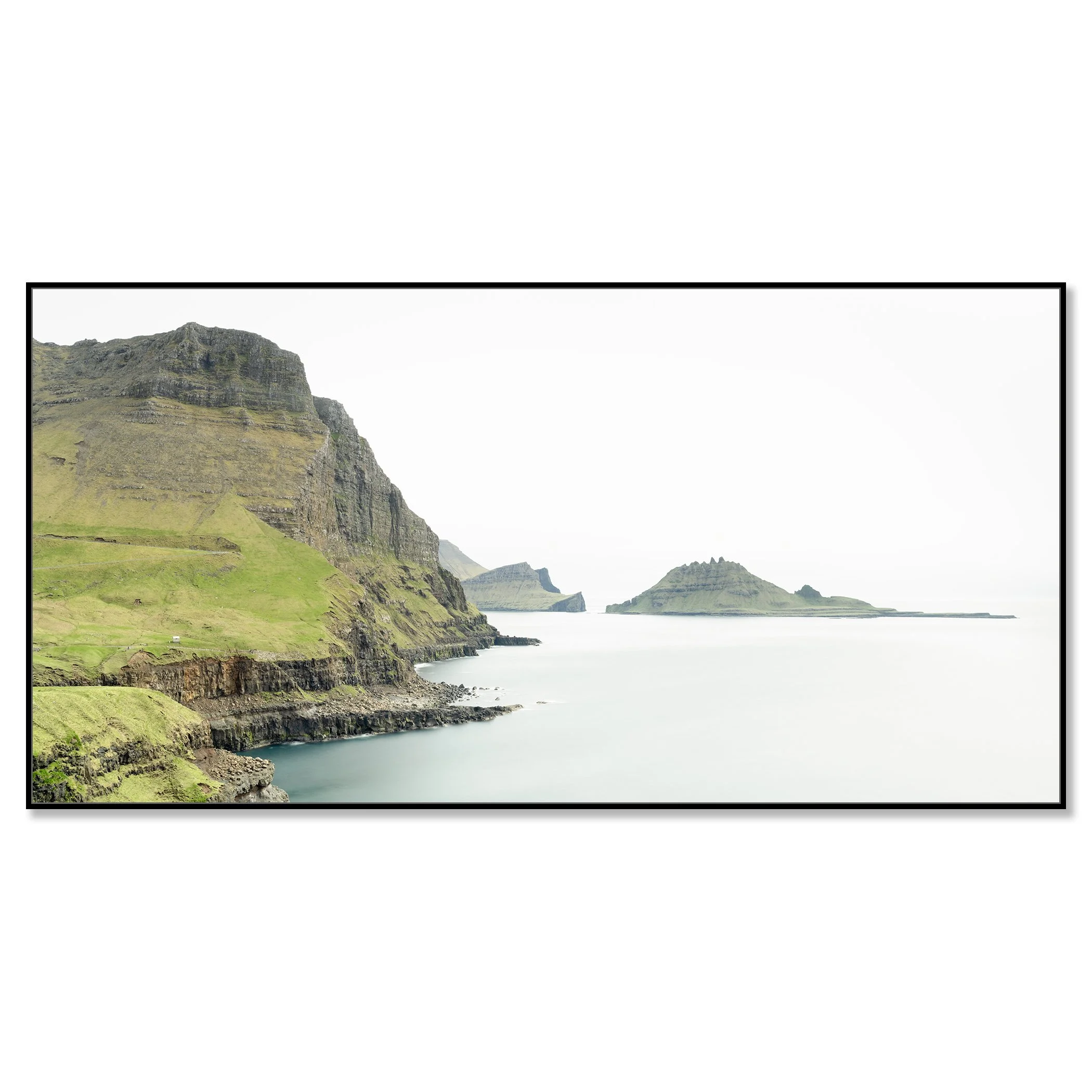 Gerald Berghammer - Color Photography. Cliffs and green hills along a body of water, with distant islands or landmasses in the background under a cloudy sky. Chromaluxe framed black