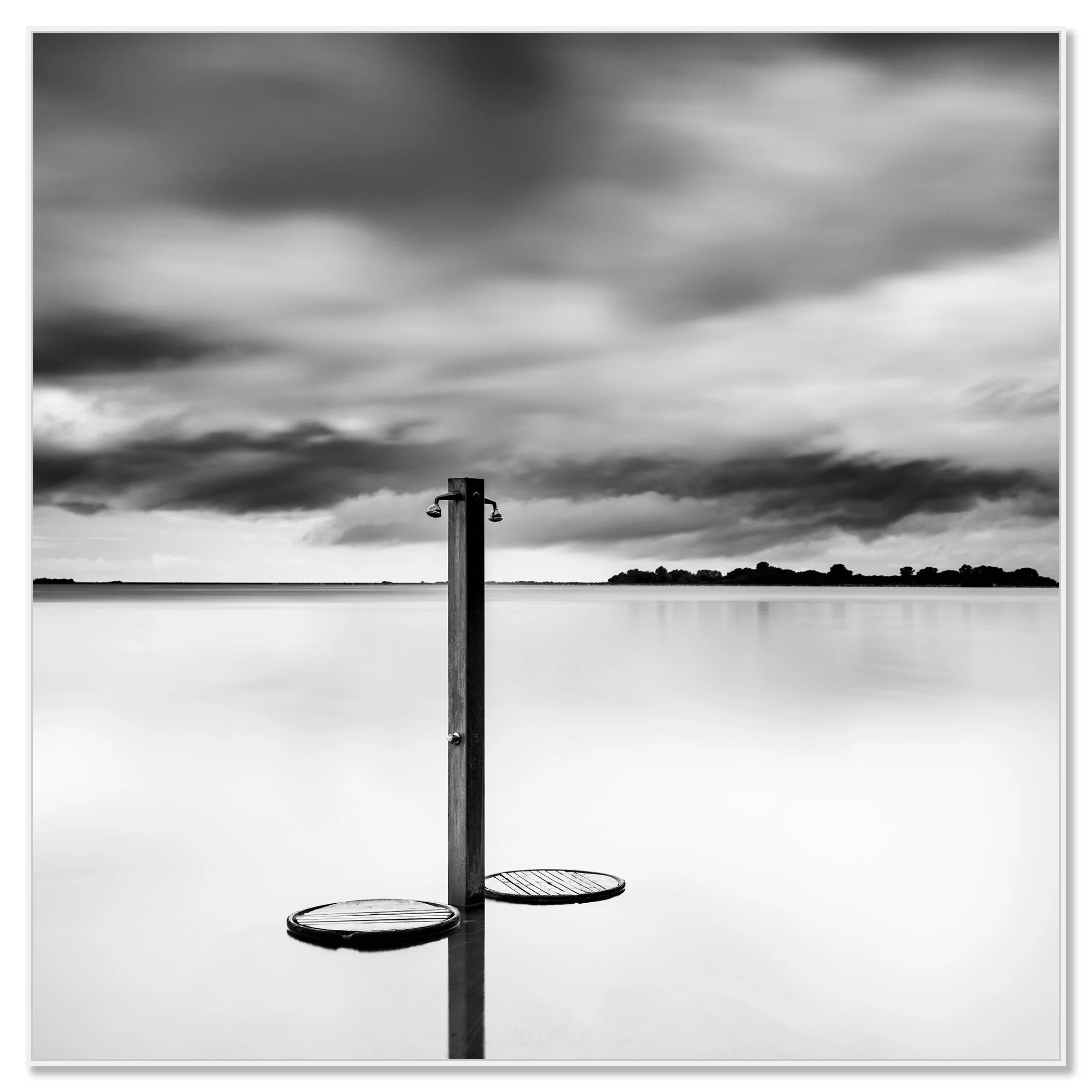 Black-and-white photo of a beach shower standing in calm water under dramatic storm clouds – framed ArtBox white