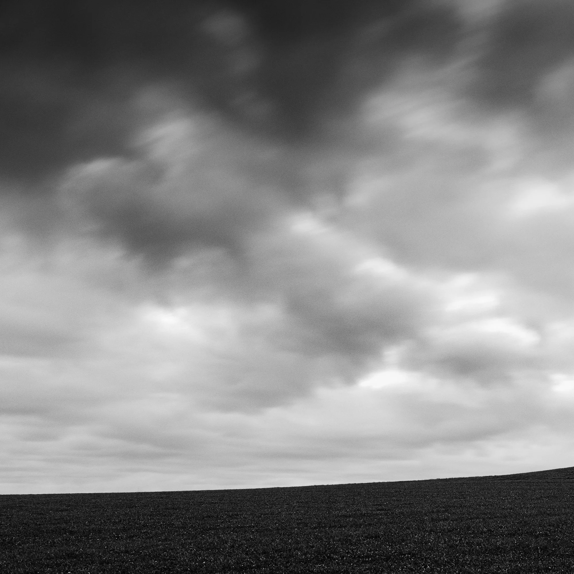 Gerald Berghammer - Black and white panorama landscape photography. A cloudy sky over a hill on a farmland with a single tree on the horizon. Print detail 1