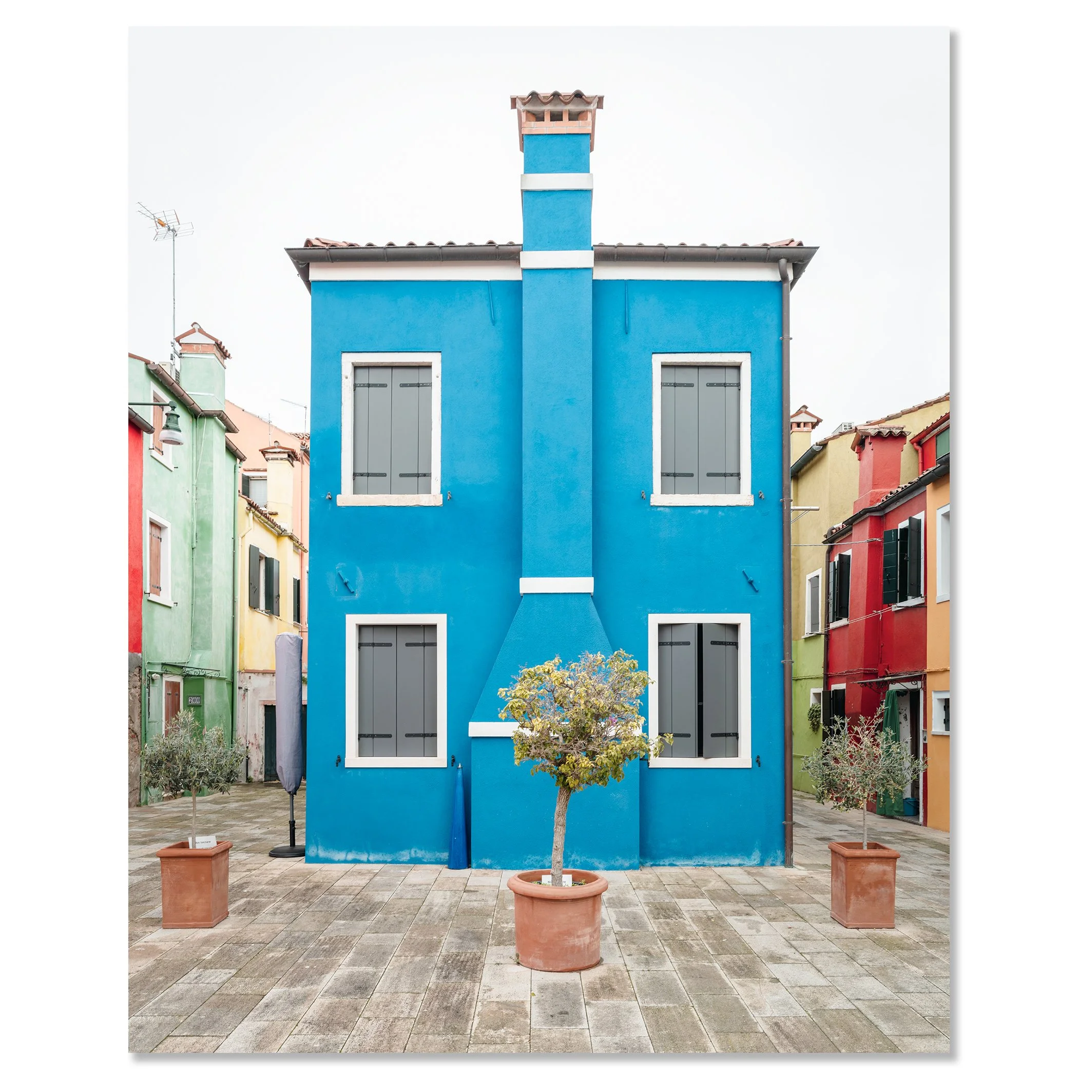 © 2025 Gerald Berghammer - Color cityscape photo. Colorful row houses with a prominent blue house in the center, potted small trees in front, and a paved courtyard. Chromaluxe frameless