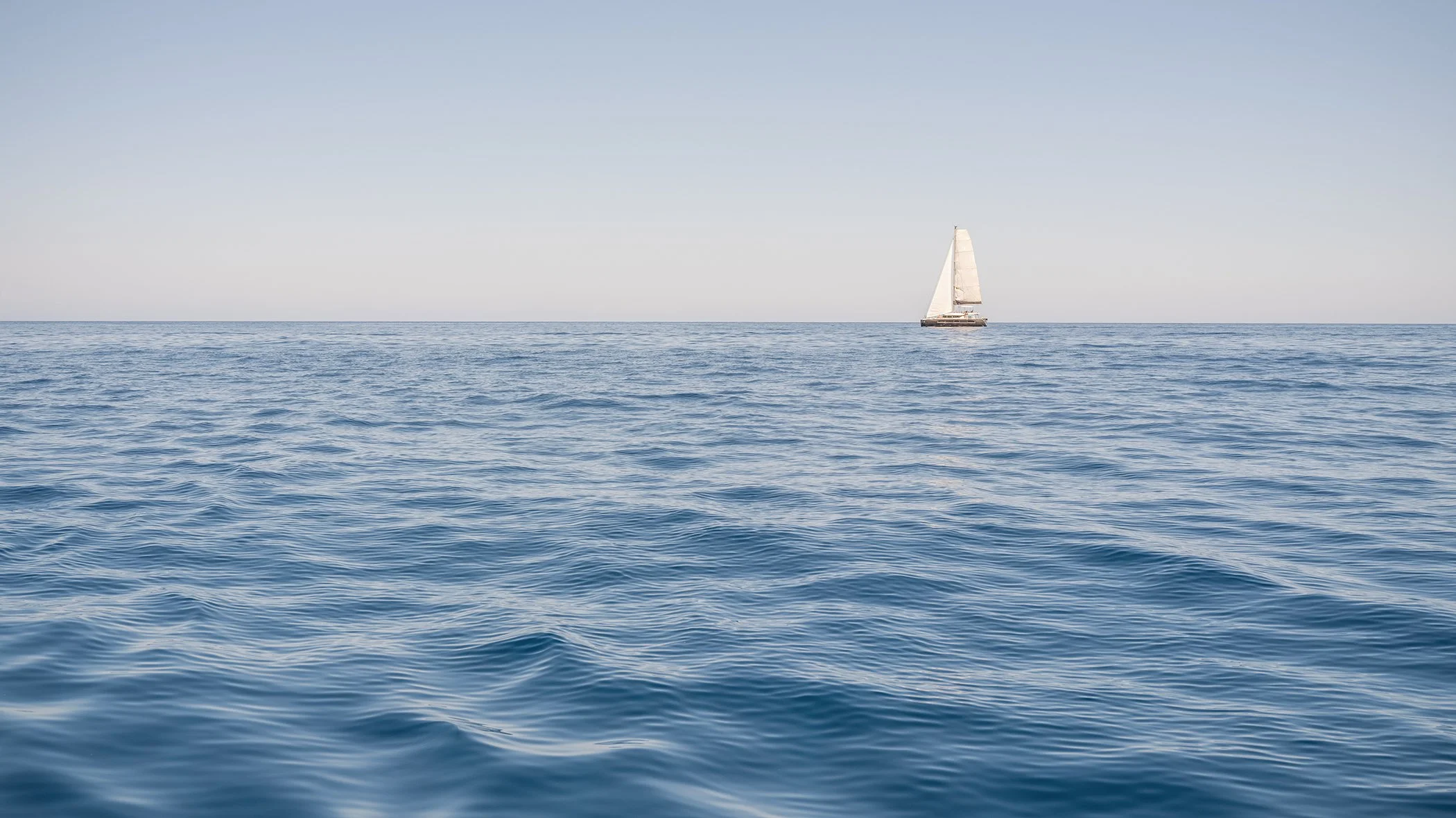 The Sound of the Sea Study 1 by Gerald Berghammer, minimalist colour photograph of a solitary sailboat on a calm blue sea beneath an open sky in Spain.