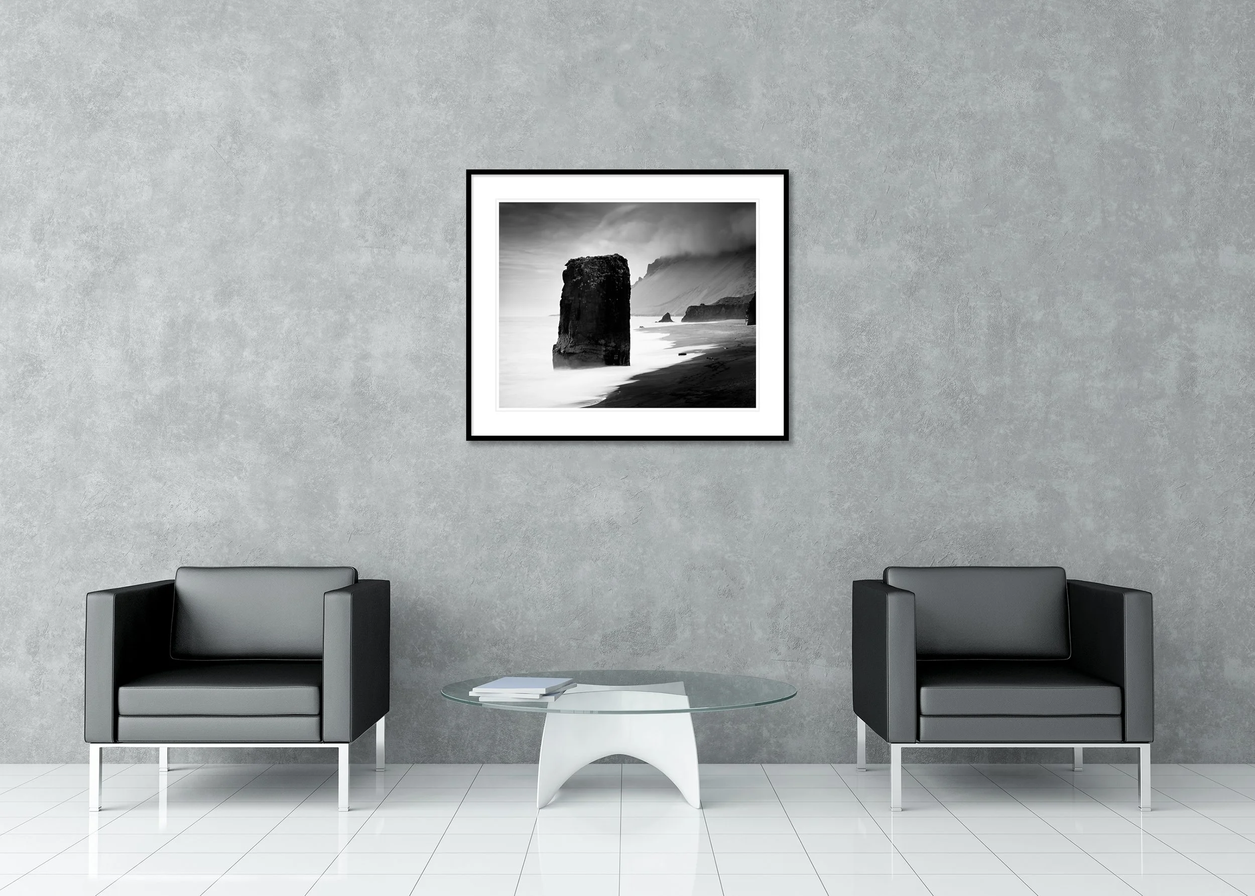 Black-and-white long-exposure rock monolith in the sea off Iceland’s foggy coast, dark sand and misty water, archival pigment print in a classic frame with mount